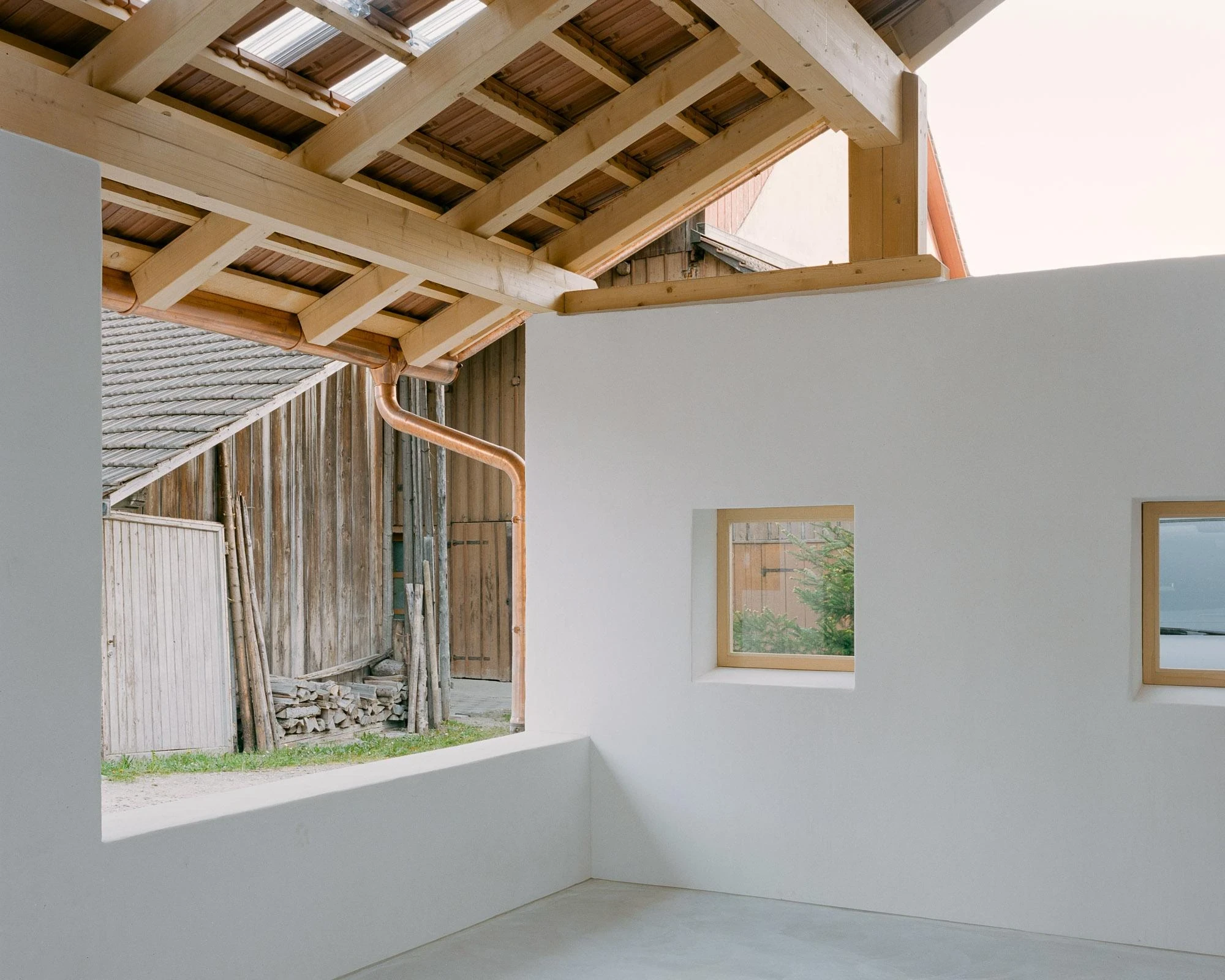 Barn Conversion in Hettlingen by Orso Dettling, photographed by Jeremiah Schwery — Terrace interior with copper downpipe traced down a white render wall, small punched windows framing the weathered barn opposite