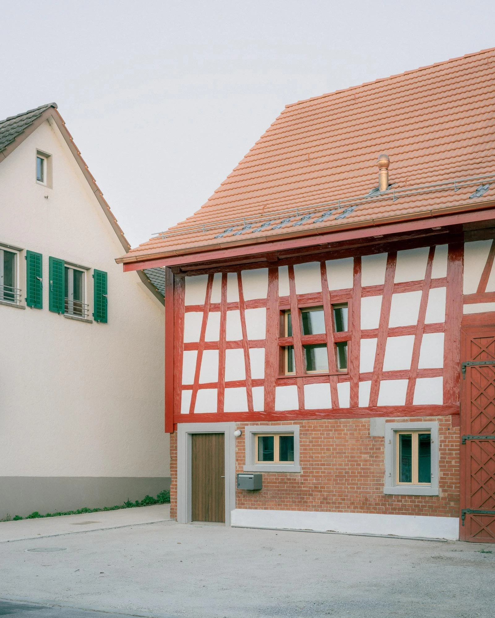 Barn Conversion in Hettlingen by Orso Dettling, photographed by Jeremiah Schwery — Neighbouring half-timbered farmhouse with red lattice frame and tile roof, the village fabric the conversion answers to