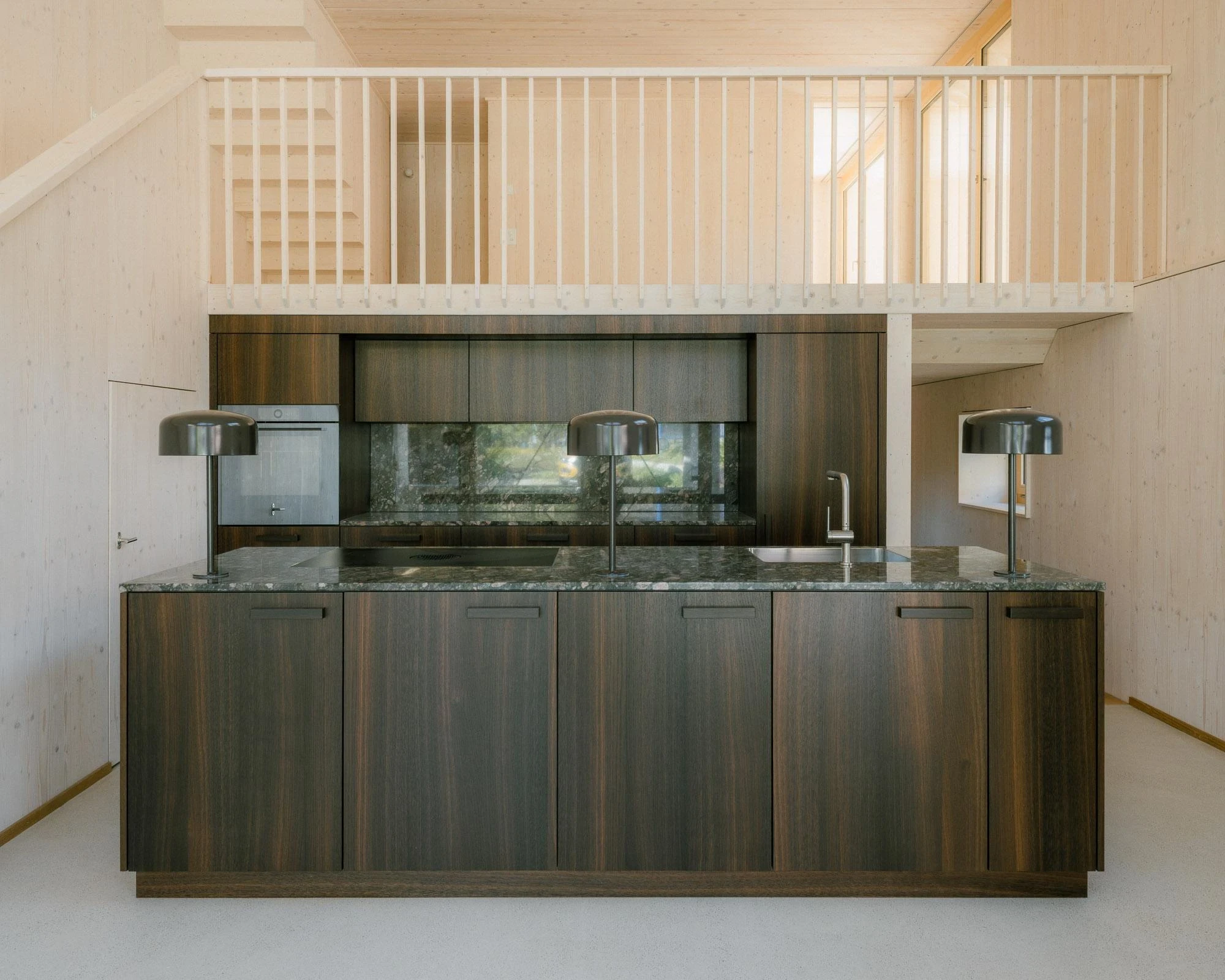 Barn Conversion in Hettlingen by Orso Dettling, photographed by Jeremiah Schwery — Kitchen detail with green-veined granite worktop, fluted spruce balustrade and a slim slot showing the gallery floor above