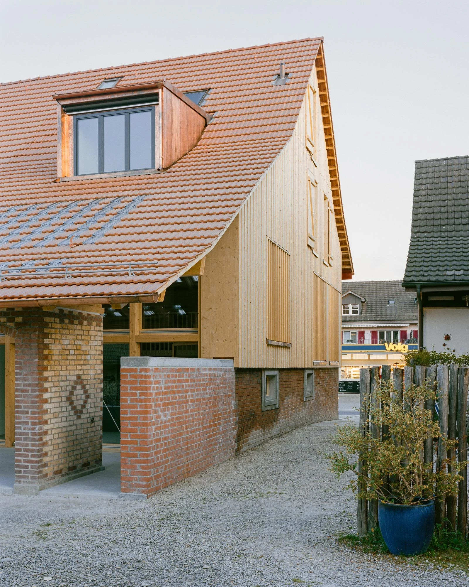 Barn Conversion in Hettlingen by Orso Dettling, photographed by Jeremiah Schwery — Street elevation of the converted stable barn at dusk, tiled roof and new vertical timber cladding meeting the brick parapet of the original walls
