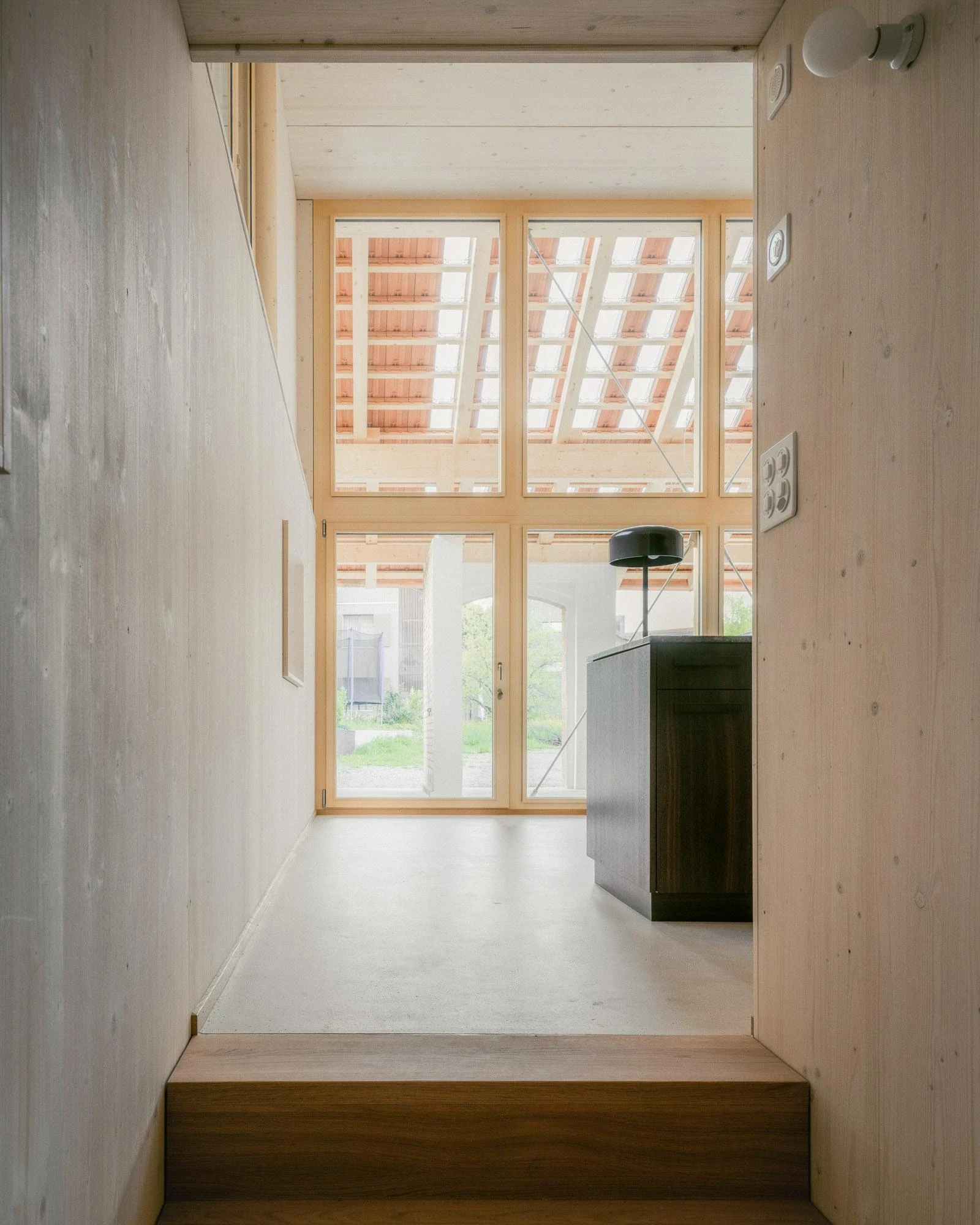 Barn Conversion in Hettlingen by Orso Dettling, photographed by Jeremiah Schwery — Corridor leading from the entrance toward the dining room, full-height glazing carrying daylight from the rafter line above to the cement floor