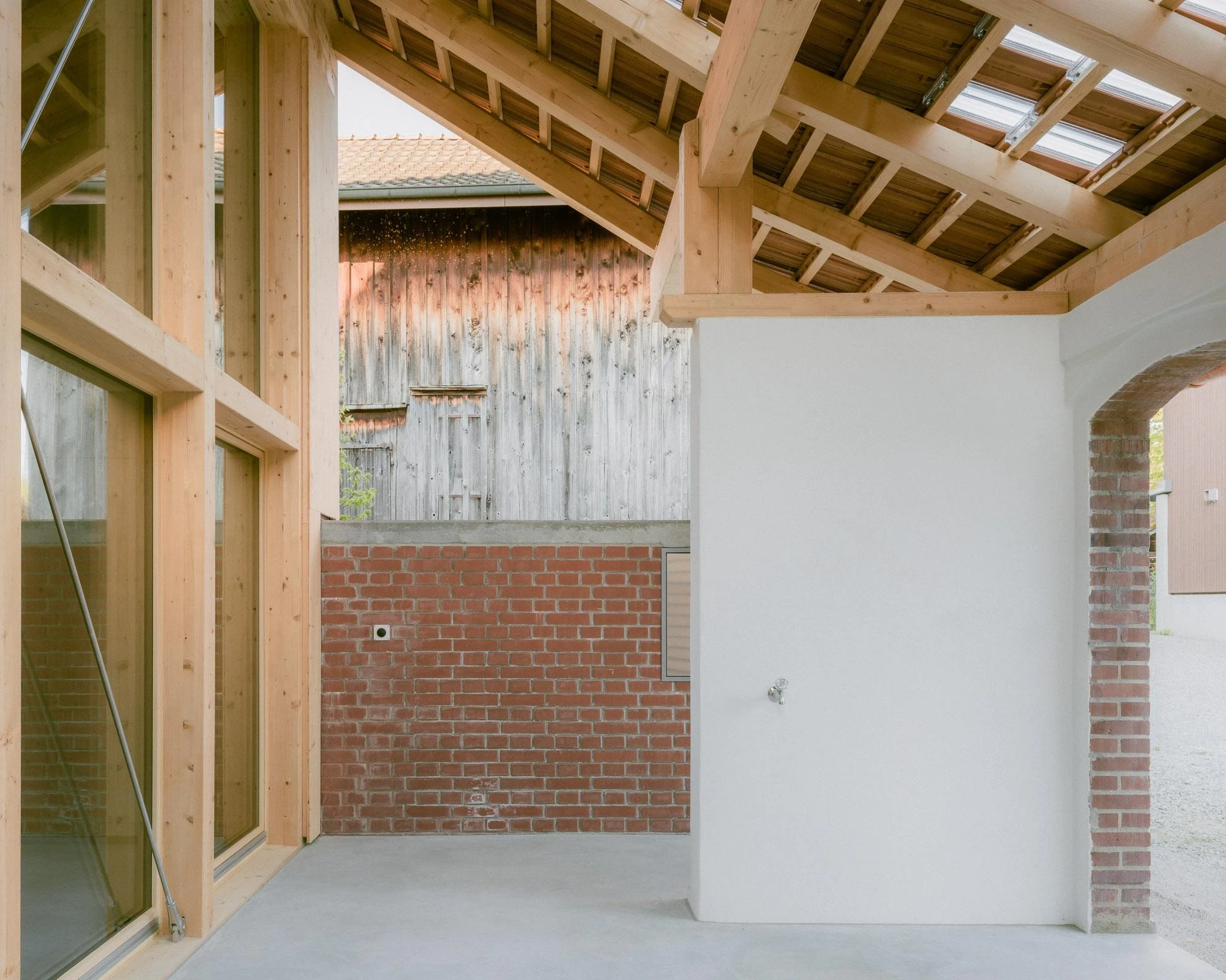 Barn Conversion in Hettlingen by Orso Dettling, photographed by Jeremiah Schwery — Covered terrace where horses once stood, glass corner, exposed roof joists and a brick parapet open to the neighbouring barn