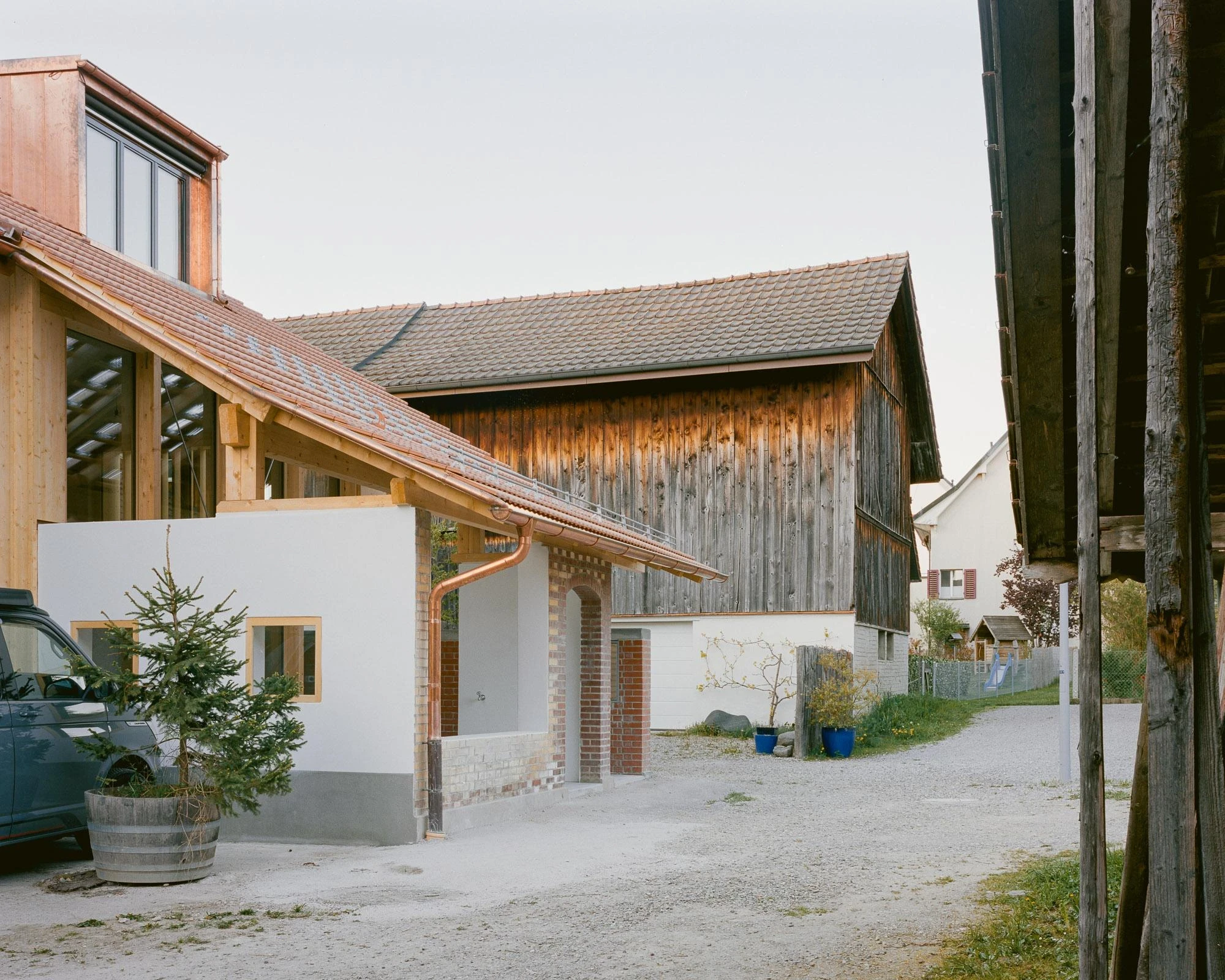 Barn Conversion in Hettlingen by Orso Dettling, photographed by Jeremiah Schwery — Rear lane view of the barn from the courtyard, weathered timber gable meeting the new white render and copper downpipe