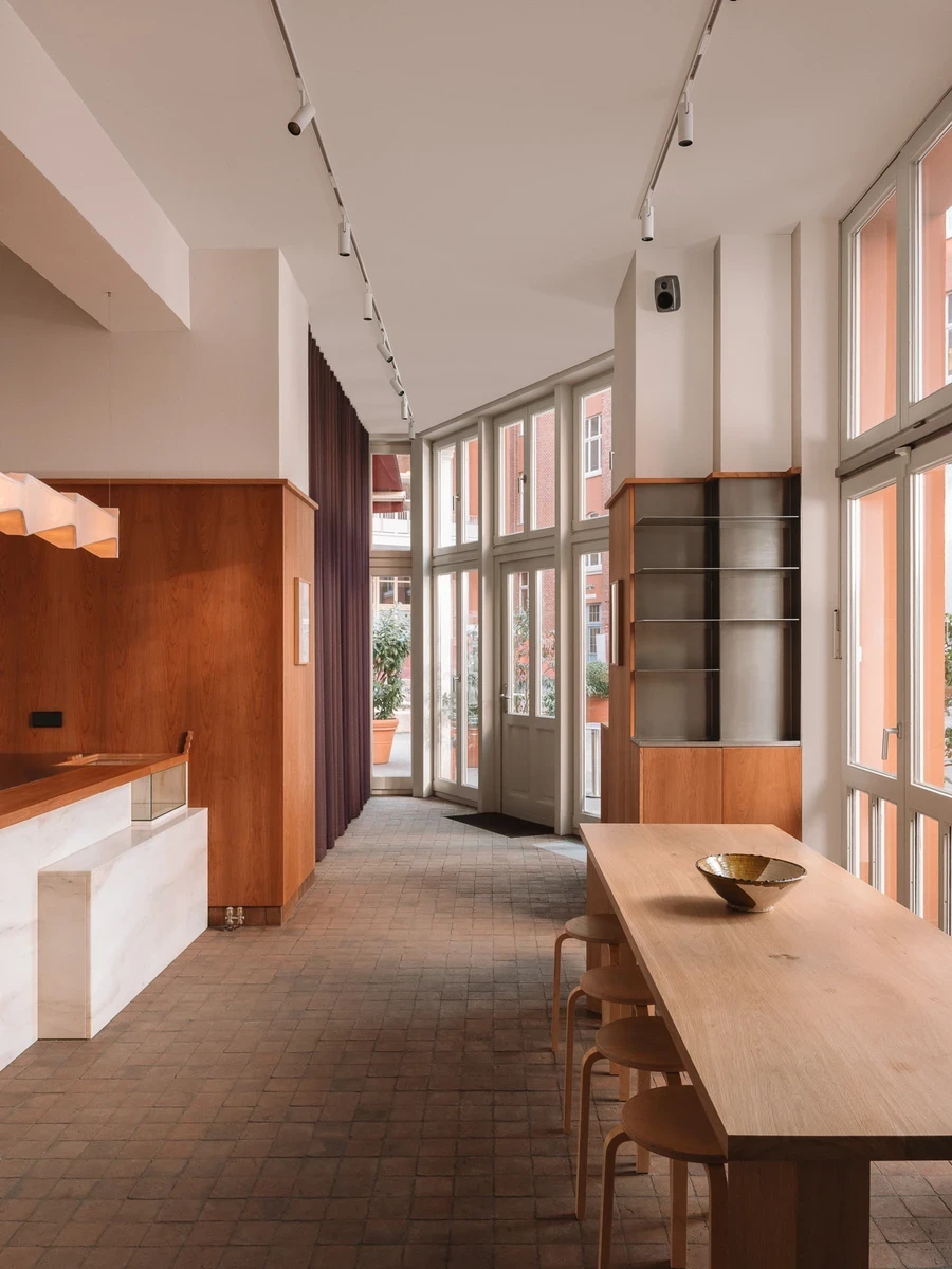 Tall casement windows open onto the 1911 courtyard with sheer aubergine curtains and a long oak table set on terracotta paver flooring.