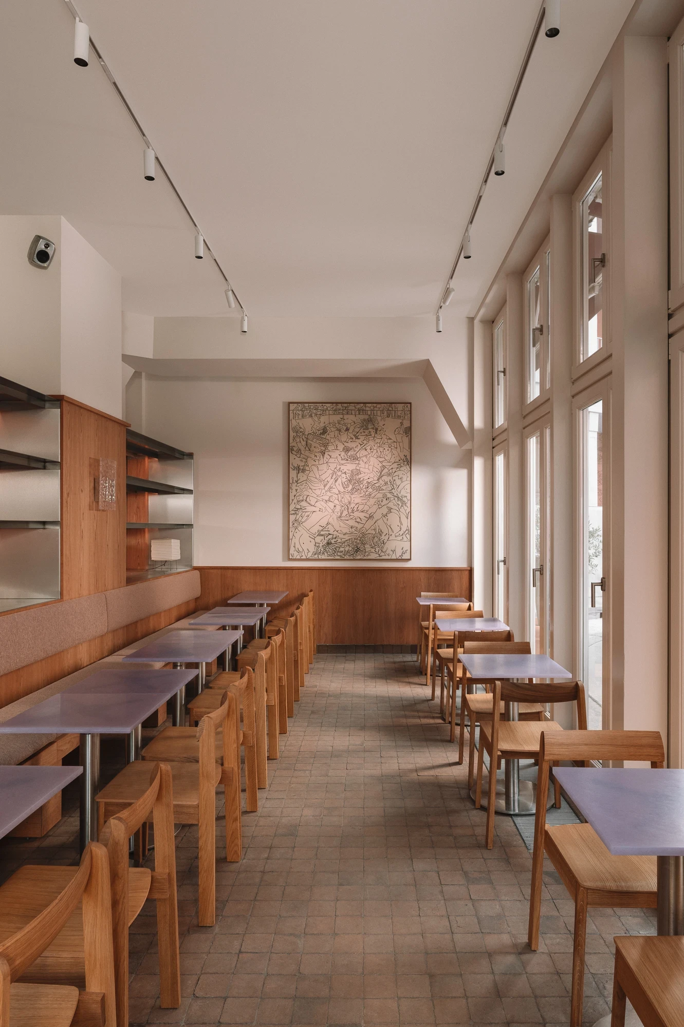 Strom Berlin by Celeste Asfour, photographed by Clemens Poloczek — Lavender resin tables and oak armchairs line the window wall with a framed city map and aubergine curtains drawn back at the far end.