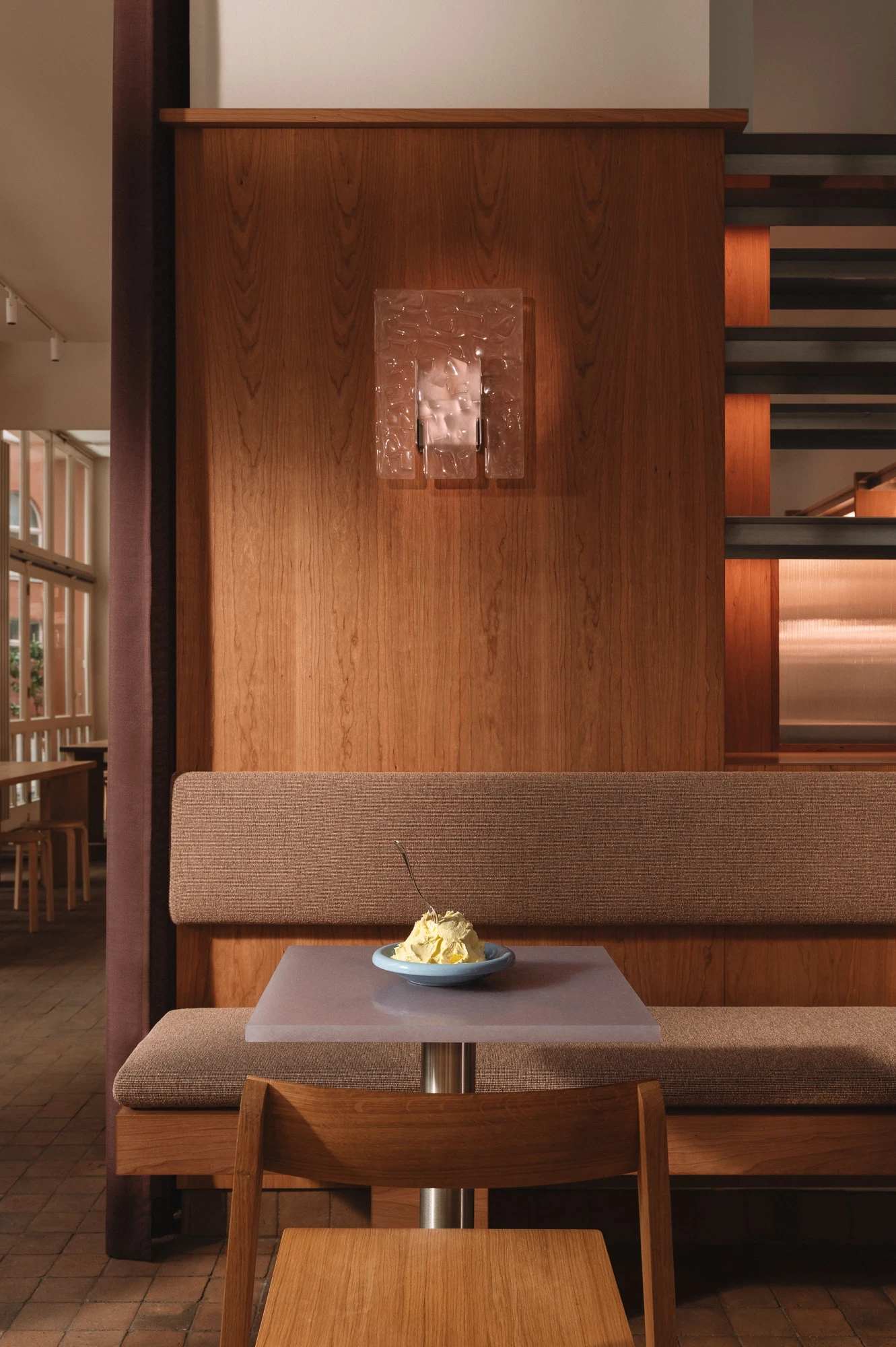 Strom Berlin by Celeste Asfour, photographed by Clemens Poloczek — A cherry-panelled banquette wall holds a hand-blown Murano sconce above a mauve bouclé bench and a lavender resin tabletop.