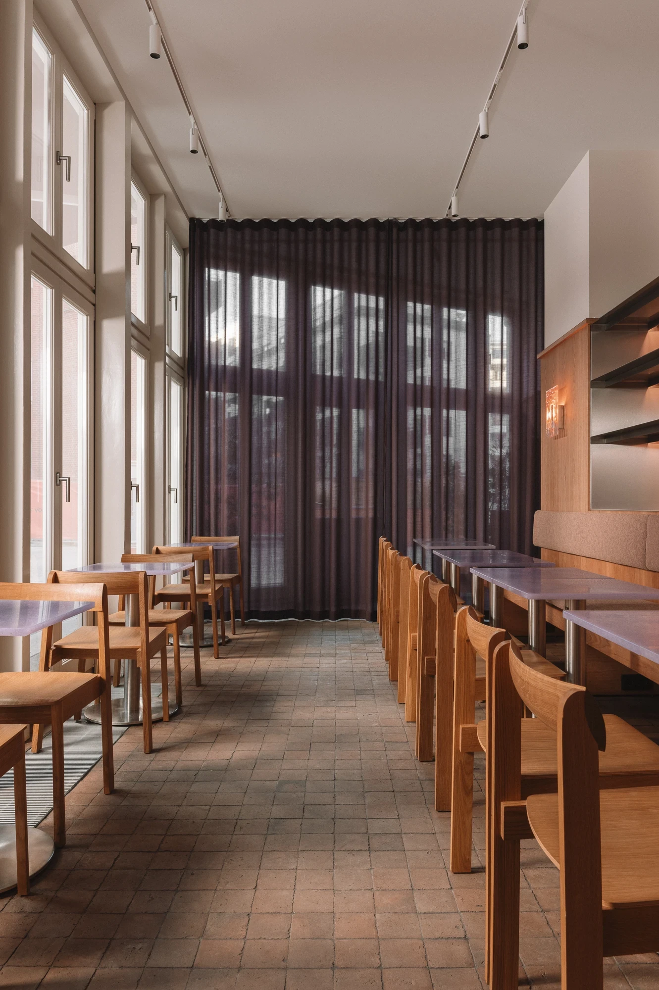 Strom Berlin by Celeste Asfour, photographed by Clemens Poloczek — A scalloped pelmet holds the aubergine curtain in soft folds with the courtyard visible through the sheer fabric and tall casement frames.