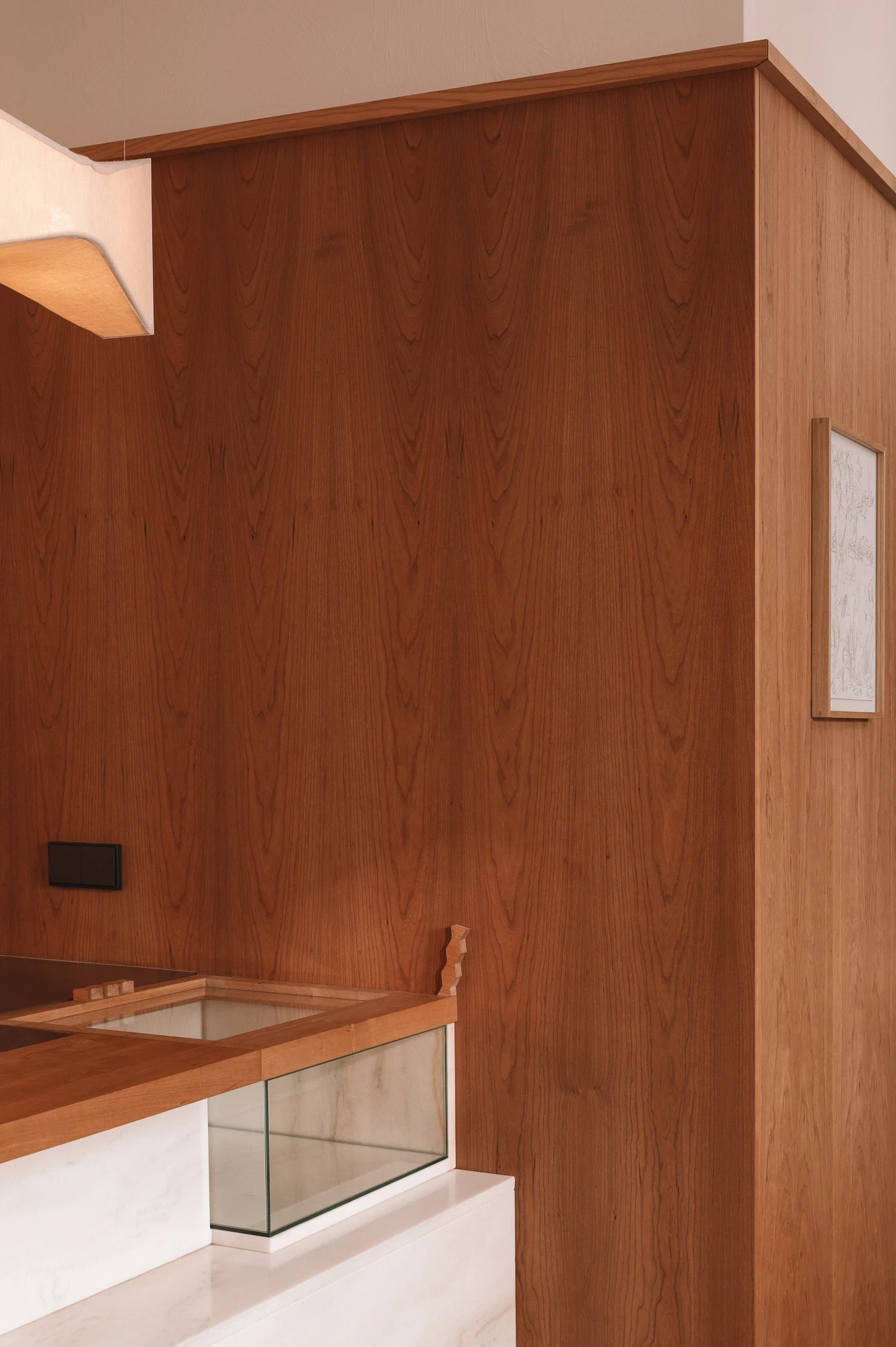 Strom Berlin by Celeste Asfour, photographed by Clemens Poloczek — Bookmatched cherry panels close the service core with a framed line drawing pinned to the side and the marble bar edge visible below.