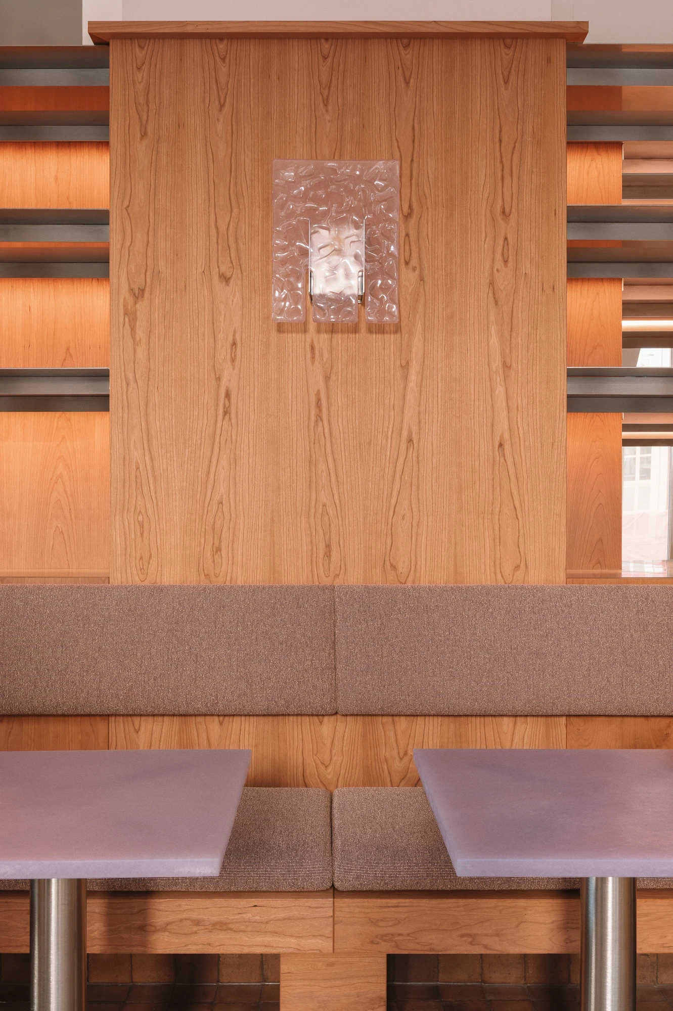 Strom Berlin by Celeste Asfour, photographed by Clemens Poloczek — A cherry-panelled partition between two banquettes holds a hand-blown Murano sconce reading like a slab of cracked clear ice.
