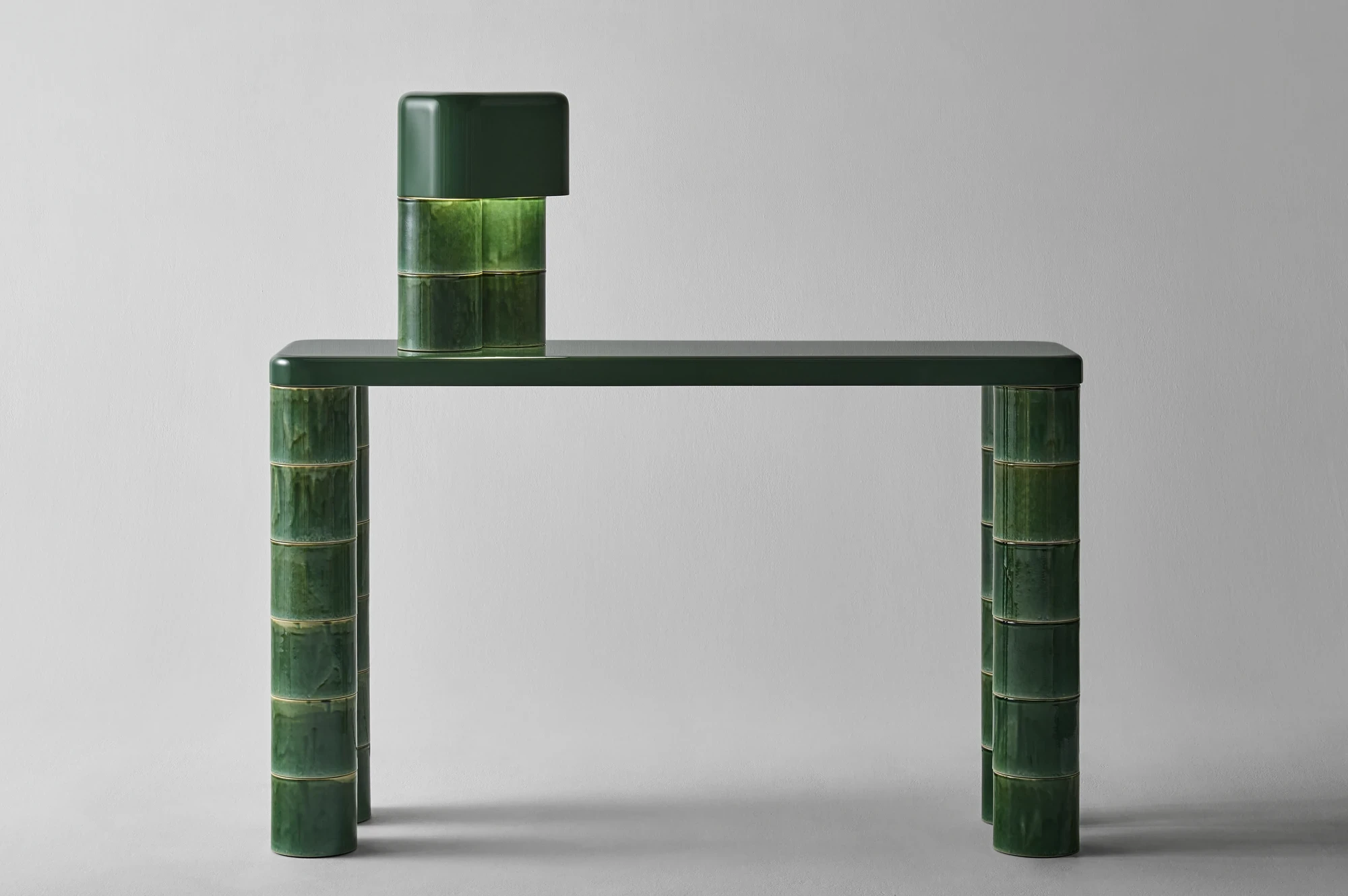 FUSHI by David Caon, photographed by Masayuki Hayashi — Cropped view of the console top and the seated lamp, showing the contrast between the smooth dark-green capping element and the runny crackled Oribe glaze of the stacked modules below