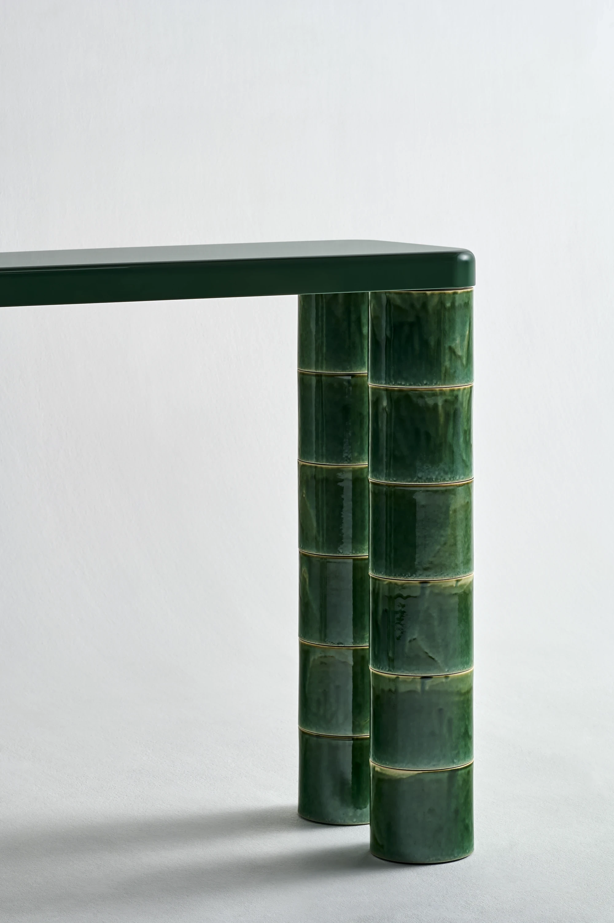 FUSHI by David Caon, photographed by Masayuki Hayashi — Tight detail of a console leg from below, the stacked Mino Yaki cylinders meeting the smooth green underside of the top in a single horizontal seam