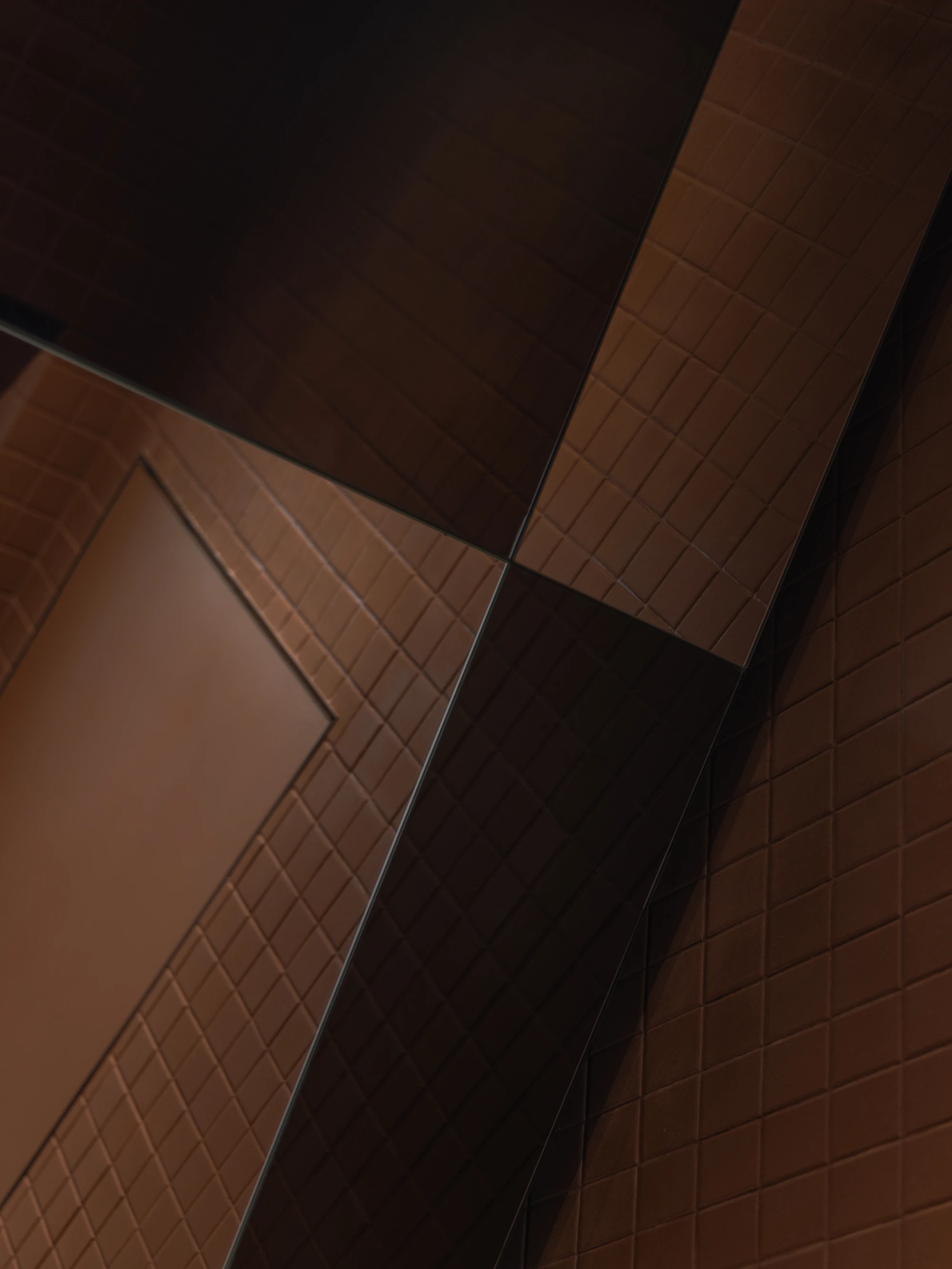 Biblioteka Coffee by Kidz, photographed by Alexander Plyaskin — an abstract overhead view of the restroom in copper-glazed square tile, broken by a black inlaid panel and a polished mirror that fractures the geometry.