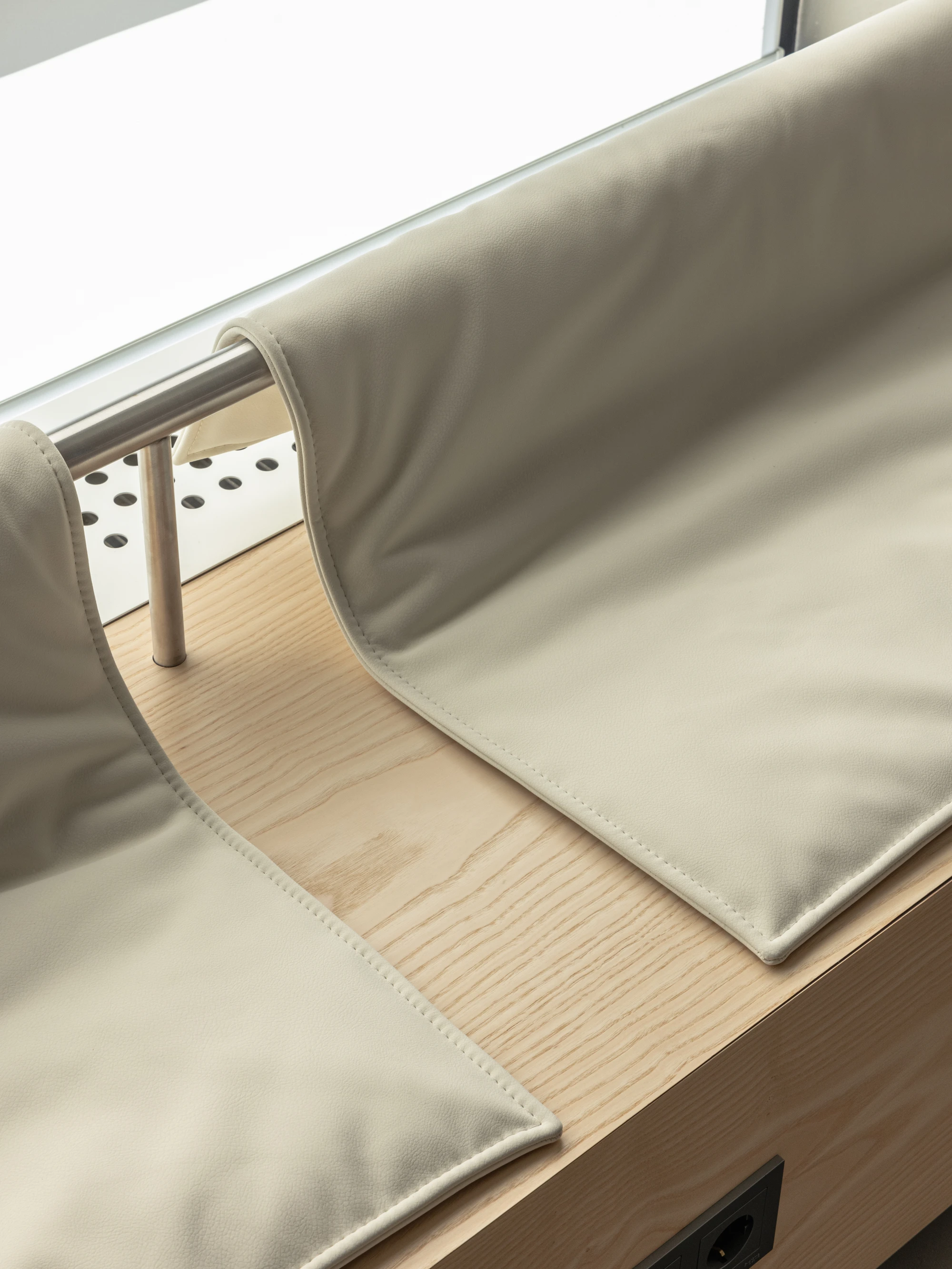 Biblioteka Coffee by Kidz, photographed by Alexander Plyaskin — a close-up of a soft beige leather cushion folded back across an ash bench top, exposing the perforated metal frame underneath.