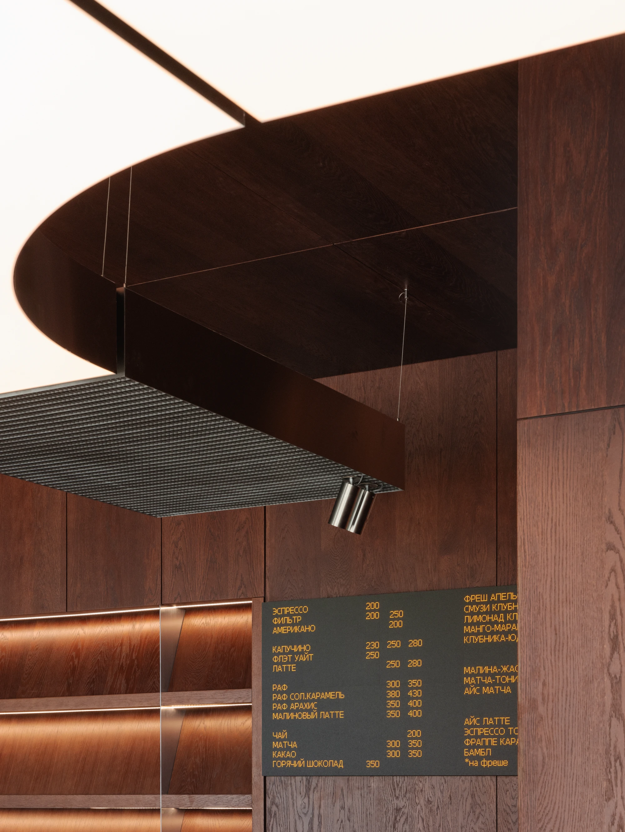 Biblioteka Coffee by Kidz, photographed by Alexander Plyaskin — an upward view of the curved steel canopy, its mud-grate underside catching warm light, with cylindrical track lamps cantilevered toward the bar below.