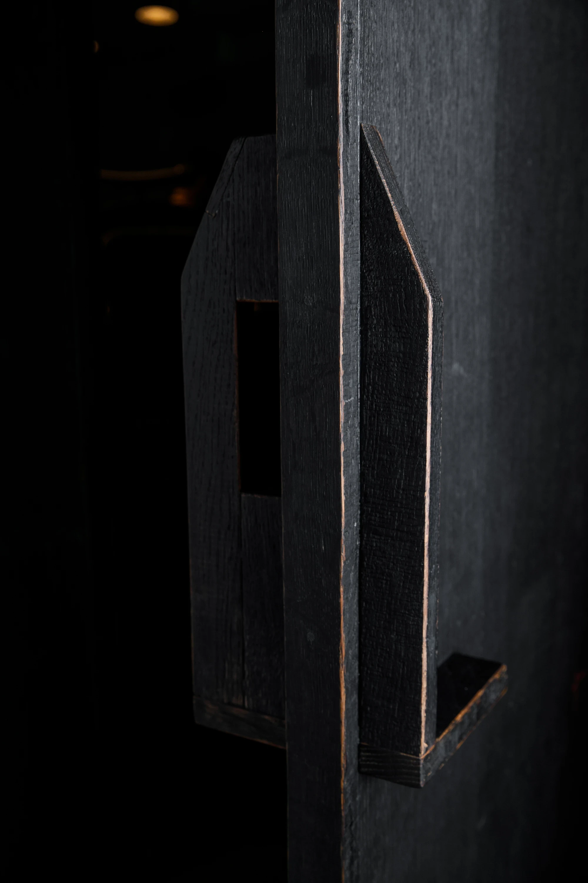 OKN Restaurant by SAGA, photographed by Daniel Annenkov — Detail of the bespoke door pull: an angular cutout handle in ebonized timber, geometric and minimal, revealing the pale timber edge at the chamfered cut.