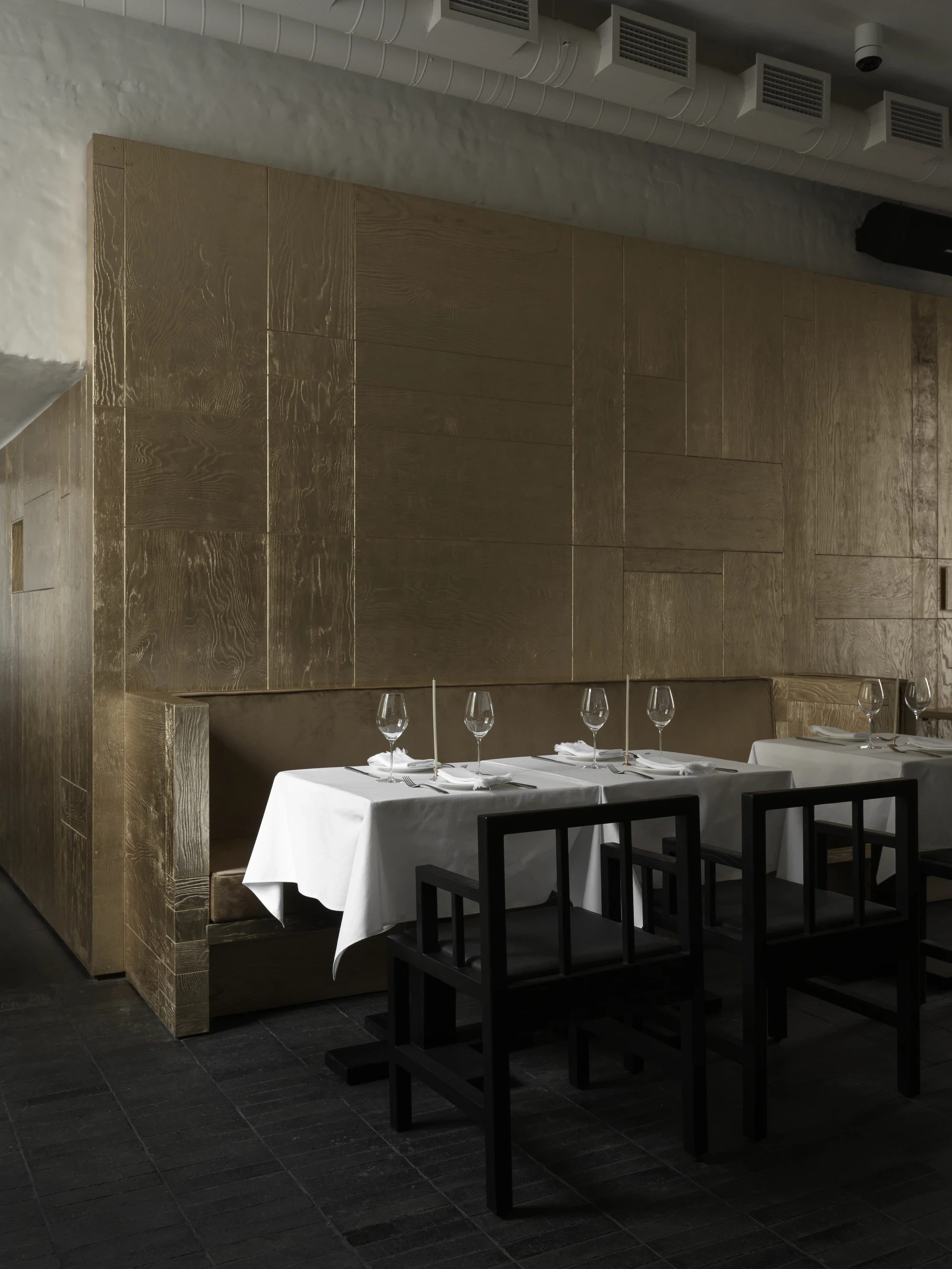 OKN Restaurant by SAGA, photographed by Daniel Annenkov — Wide view of the main dining room in daylight: rough white plaster walls with exposed brick column bases at left, gold-leaf timber panel partition at right, white linen tables set with wine glasses