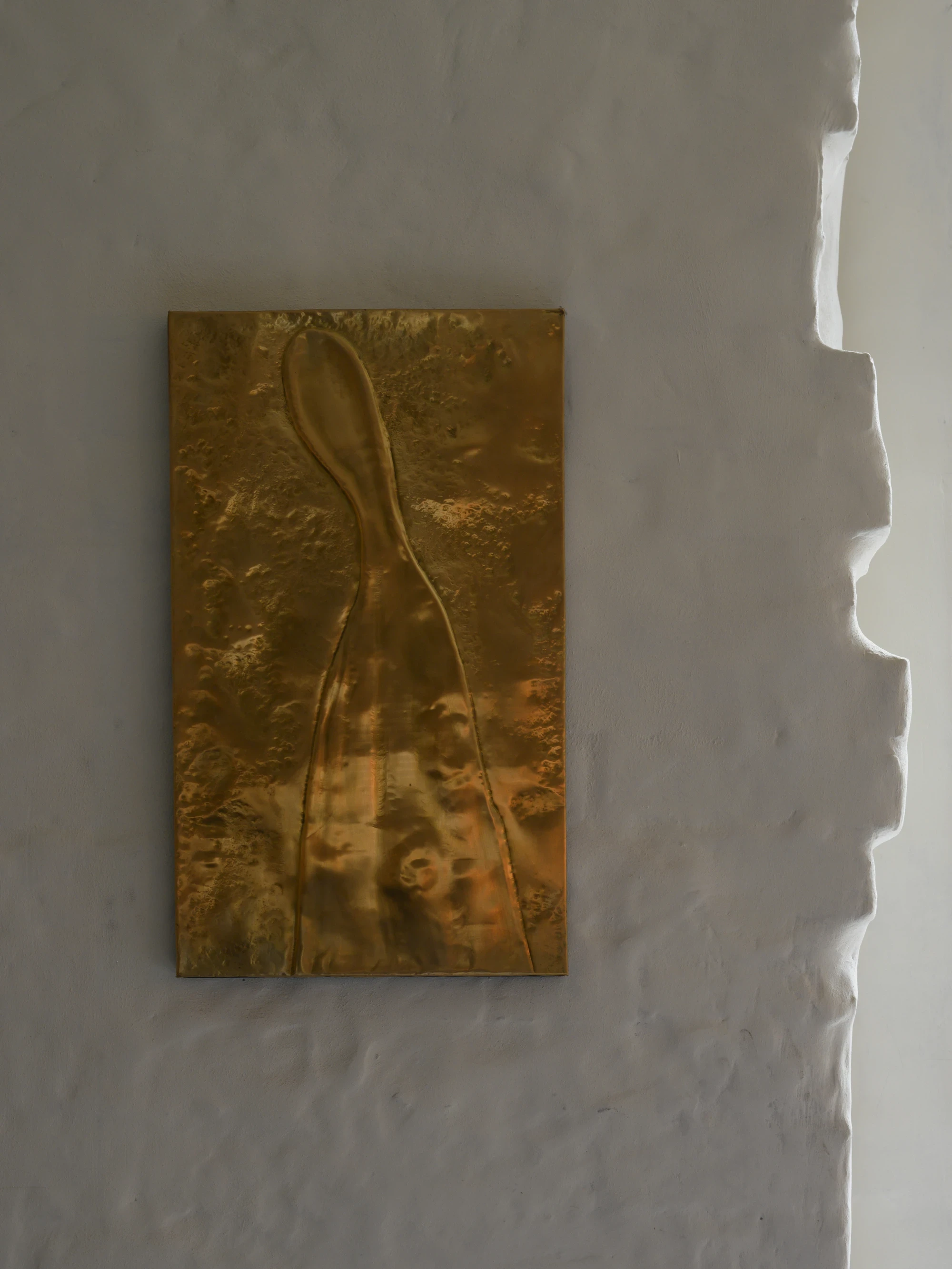 OKN Restaurant by SAGA, photographed by Daniel Annenkov — A bronze relief panel mounted on rough white plaster: a rectangular cast with a raised figurative form, its surface oxidised to a warm patina.