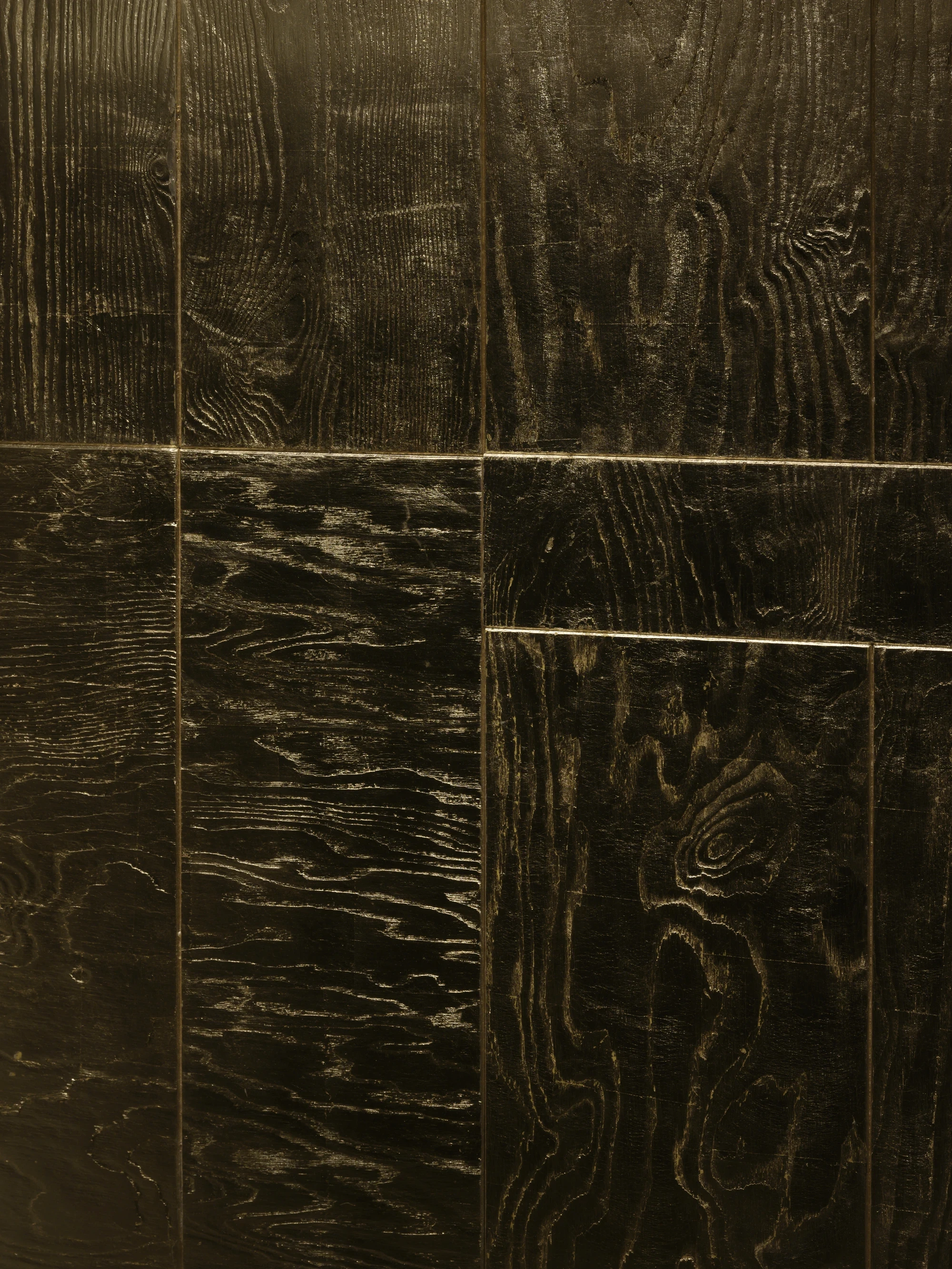 OKN Restaurant by SAGA, photographed by Daniel Annenkov — Close macro detail of the gold-leaf timber wall panels in low light: the surface shows pronounced wood grain impressed through the gold, with tonal variation from pale gold to near-black between pa