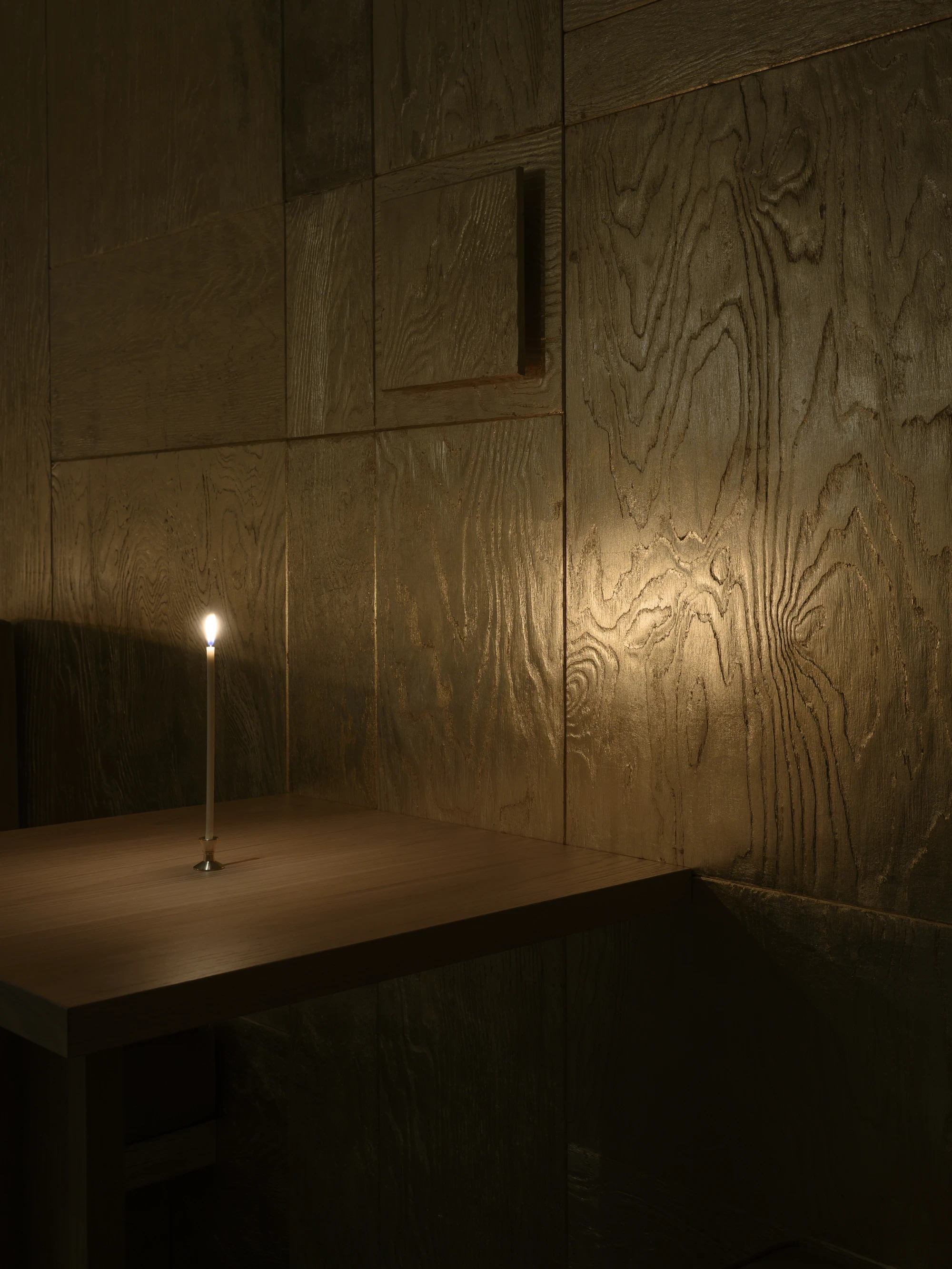 OKN Restaurant by SAGA, photographed by Daniel Annenkov — Detail of the banquette frame corner, showing the joint between gold-leaf timber cladding and olive canvas upholstery. The wood grain presses through the gold leaf at the corner.