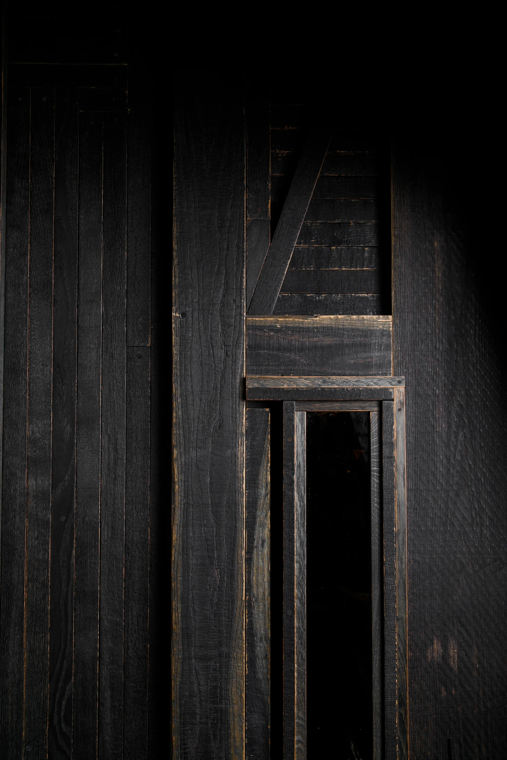 OKN Restaurant by SAGA, photographed by Daniel Annenkov — Close-up of the ebonized timber entrance door: vertical planks in near-black with visible amber grain edges, a diagonal brace element, and a narrow vertical gap at the centre forming a shadow line.