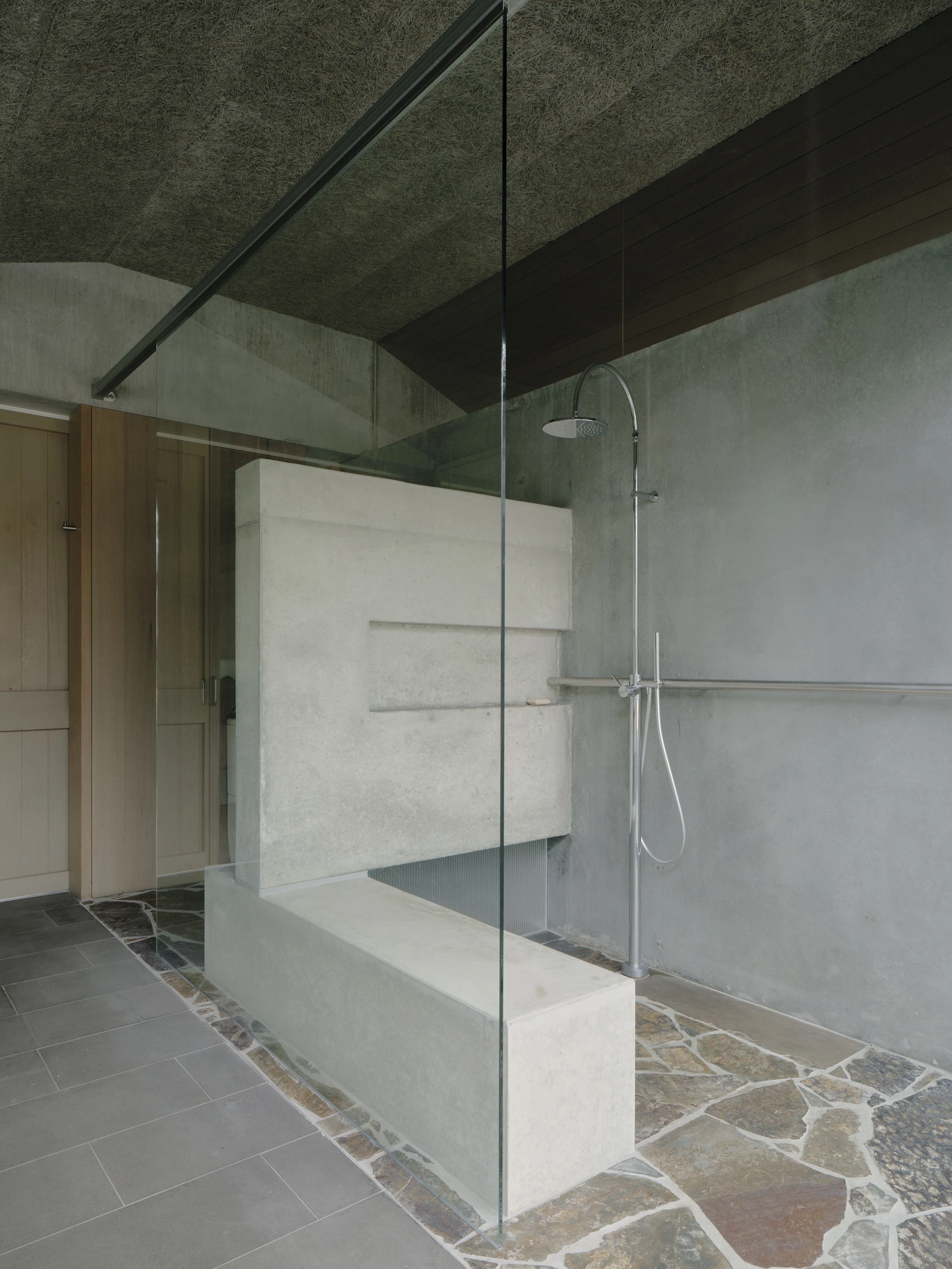 This is Lumeah by Pepper & Well, photographed by Tom Ross — The new in situ concrete partition floating between shower and toilet zone, its recessed niches reading as horizontal courses, with Mintaro Brown Back slate laid in crazy paving meeting the origi