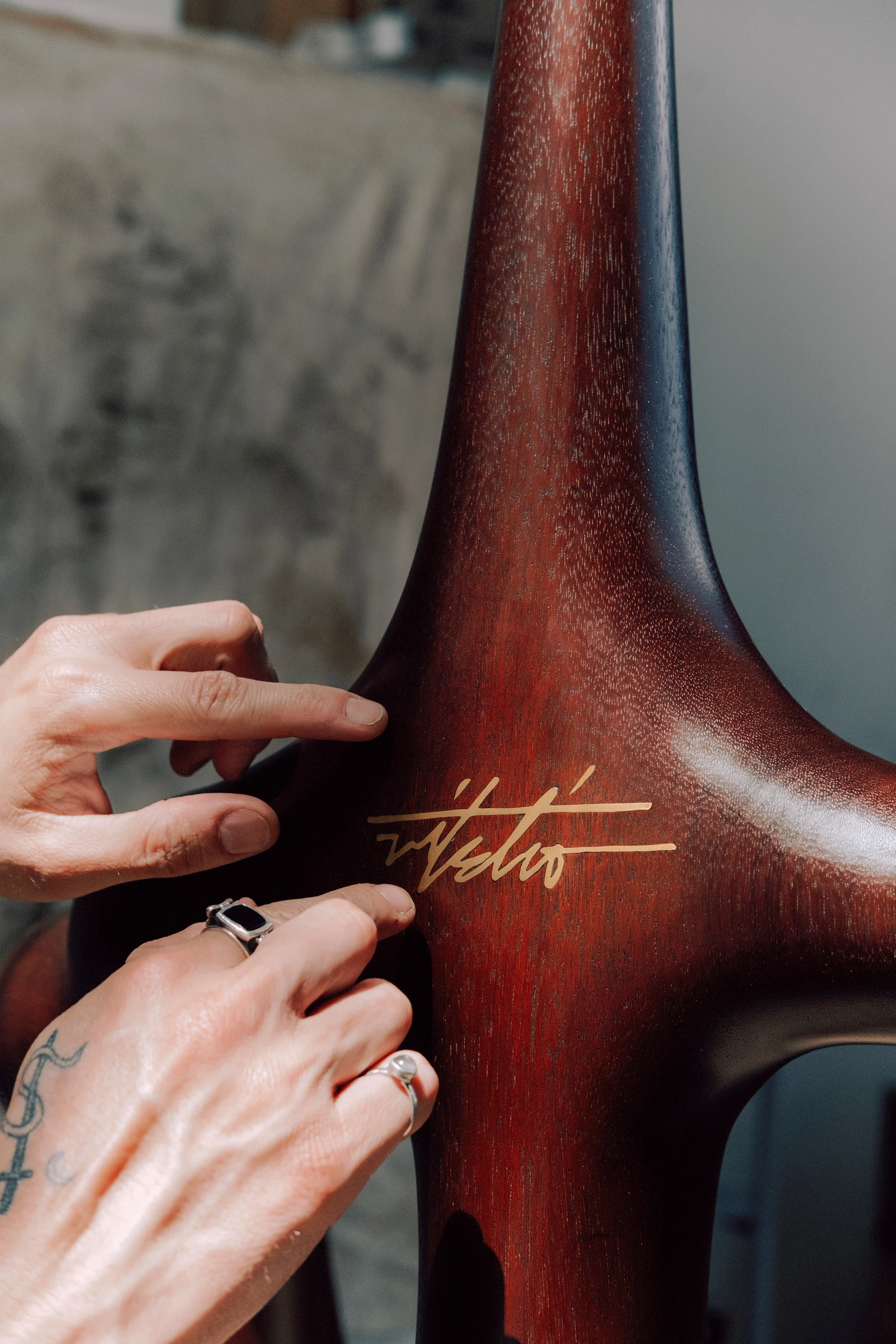 Instructions by Alberto Vitelio, photographed by @_victorjacques — two tattooed hands sign the Doussié central spine in gold cursive, the fibrous reddish grain of the hand-carved wood filling the frame.