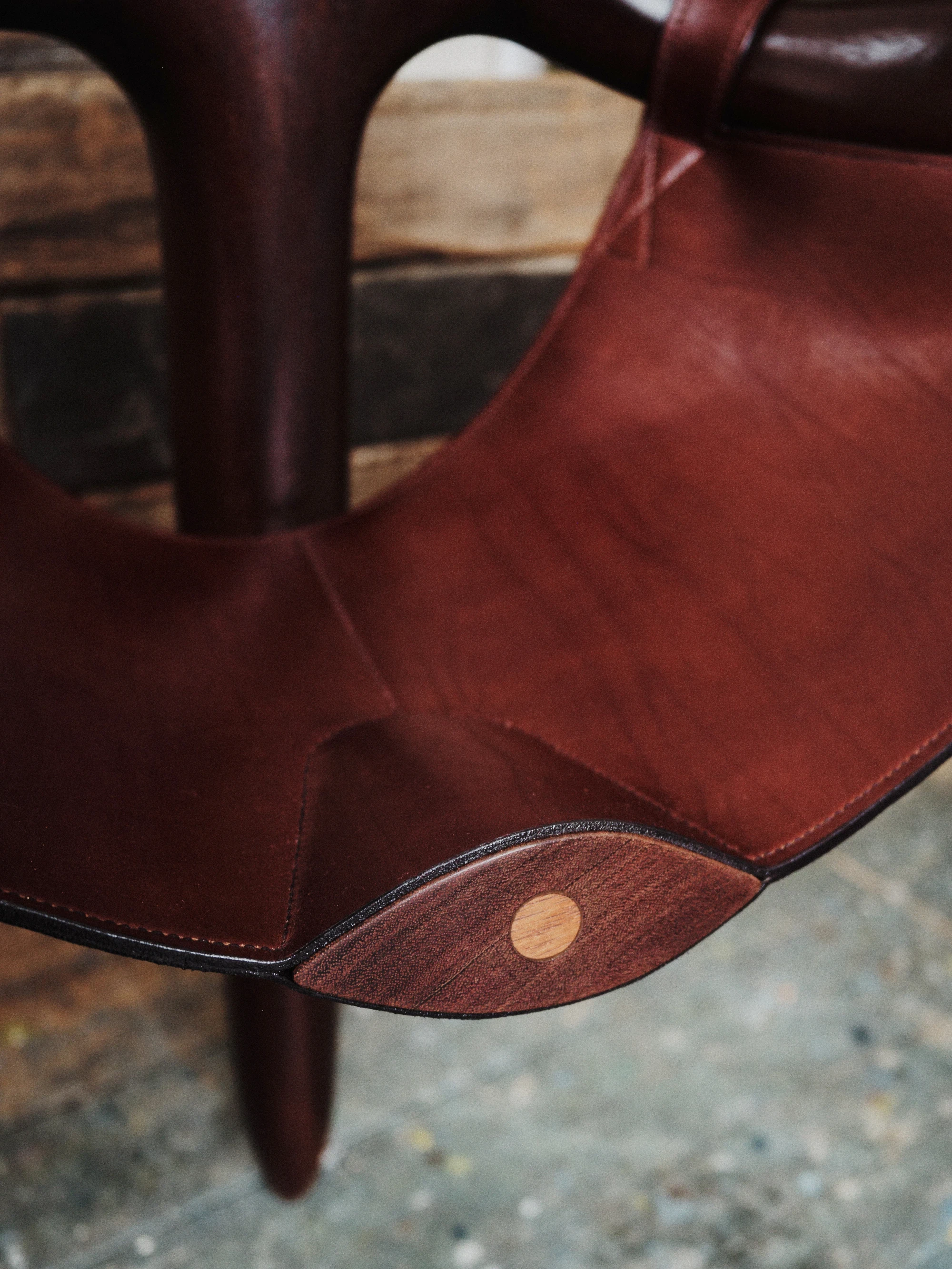 Instructions by Alberto Vitelio, photographed by @_victorjacques — close view of the leather seat corner where a circular wooden plug fastens the raw-edged, hand-stitched hide to the Doussié frame.