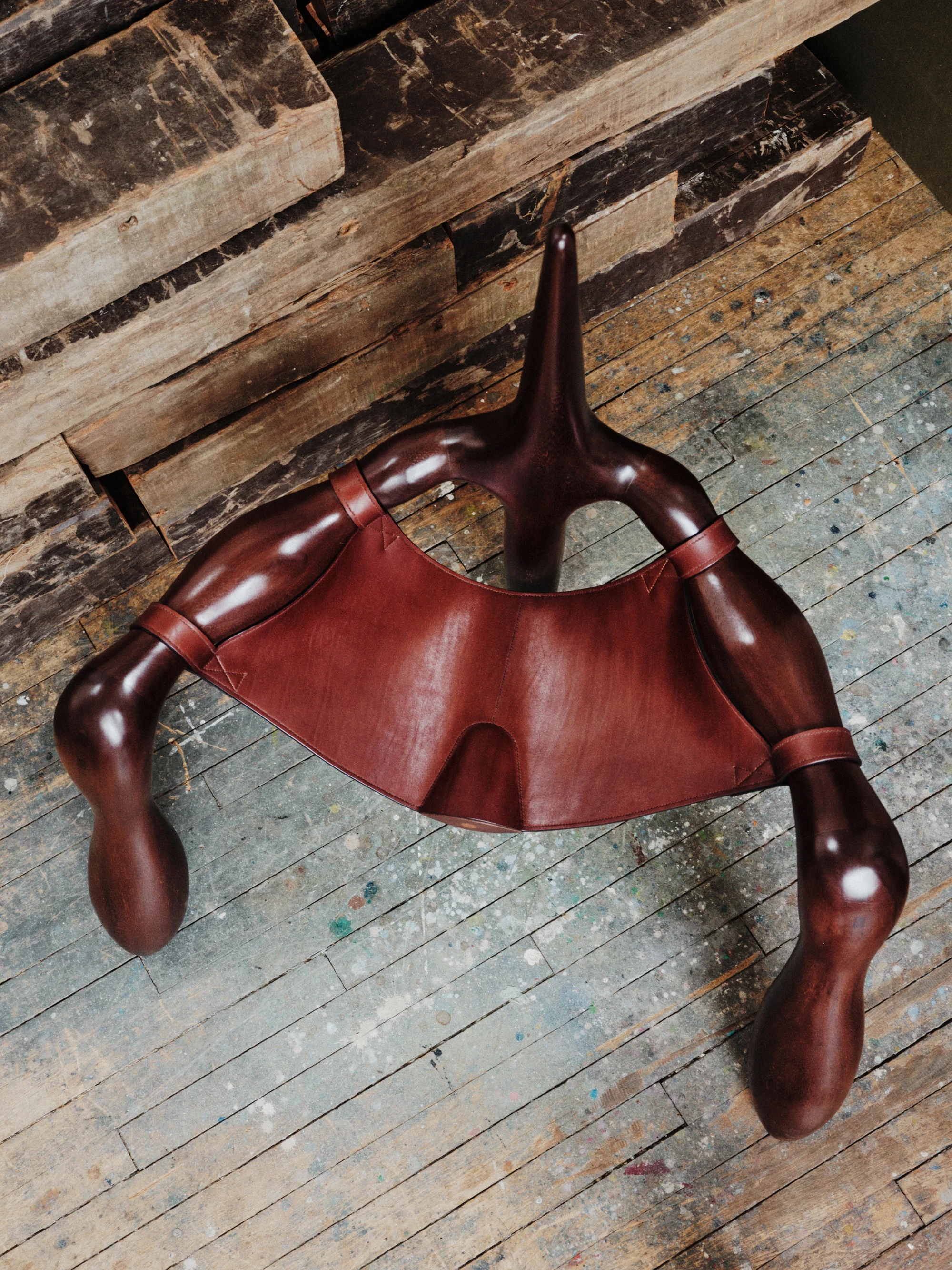 Instructions by Alberto Vitelio, photographed by @_victorjacques — overhead view of the chair on the studio floor, the tripartite leg arrangement radiating outward and the broad leather seat panel sagging gently at its center.