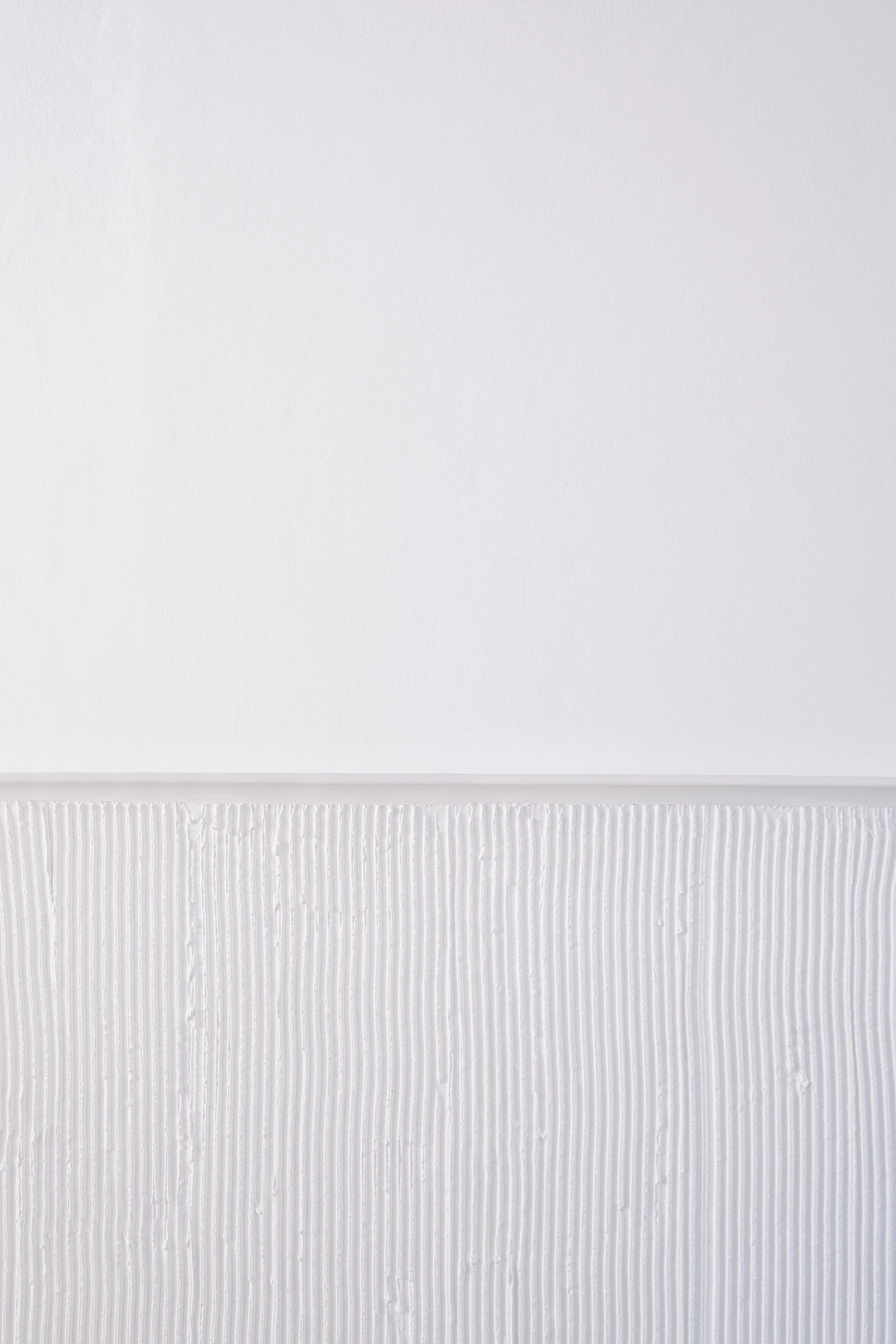 PSJ Chapel by Esteras Perrote Studio, photographed by Andrés Domínguez — close detail of the interior wall junction: smooth white plaster above and a vertically striated fine-ribbed render wainscot below, the two textures separated by a thin shadow line.