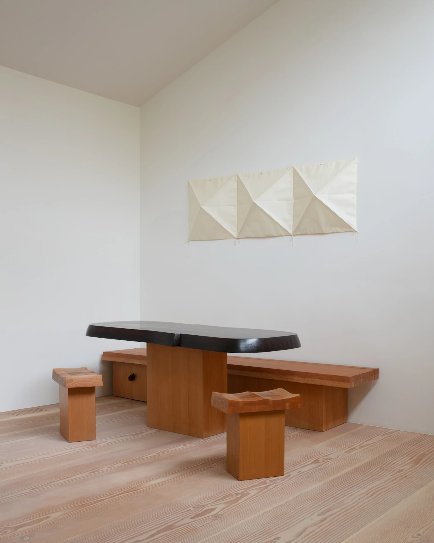 Studio & Guest House by Neil Logan, photographed by Mikael Olsson — an ebonized-top live-edge table with fir bench seating occupies the studio's lower level, a folded canvas wall piece pinned to the white plaster above, pale fir plank flooring below.