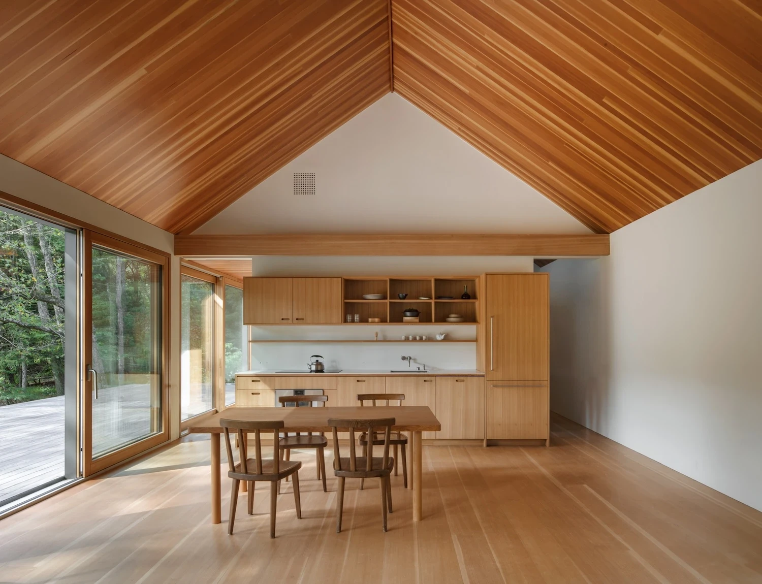 Studio & Guest House by Neil Logan, photographed by Mikael Olsson — the guest house kitchen and dining area beneath a cedar tongue-and-groove vaulted ceiling: fir cabinetry runs the back wall, a large sliding door opens to a timber deck.