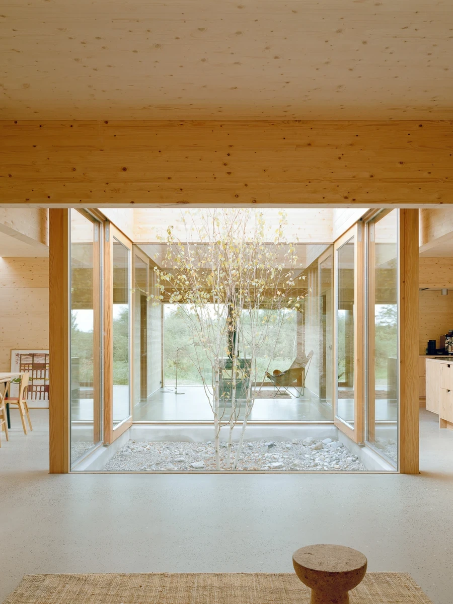 House in Ebeltoft by Høyer Arkitektur — Ebeltoft, Denmark: On a glacial plateau at the edge of Ebeltoft, Høyer Arkitektur completes House in Ebeltoft, a timber-panel family house centered on an atrium of gravel and glass open to all four compass points.