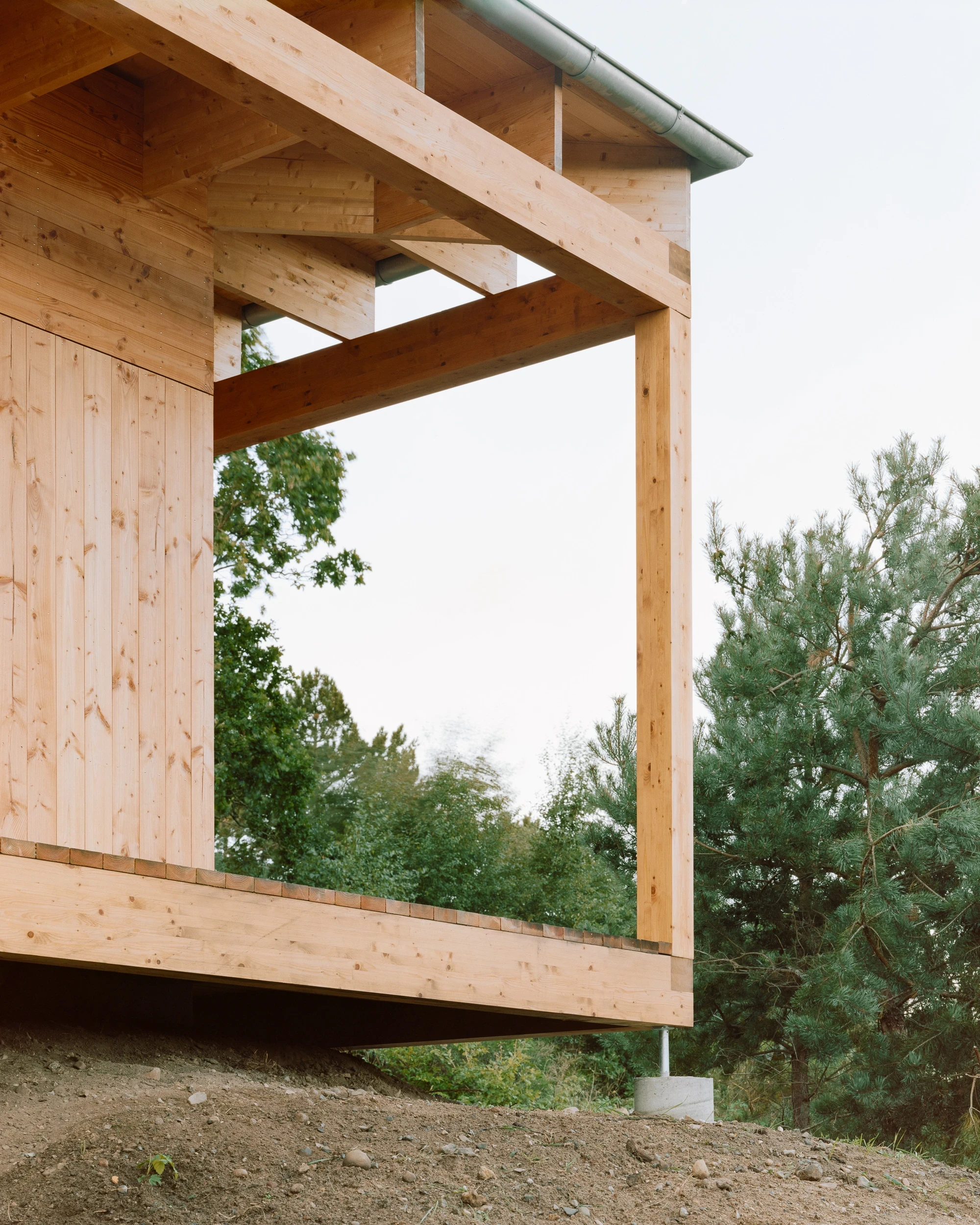 House in Ebeltoft by Høyer Arkitektur, photographed by Hampus Berndtson — close detail of the colonnade corner, showing the laminated spruce beam-to-column joint and green patinated steel gutter above the moraine soil.