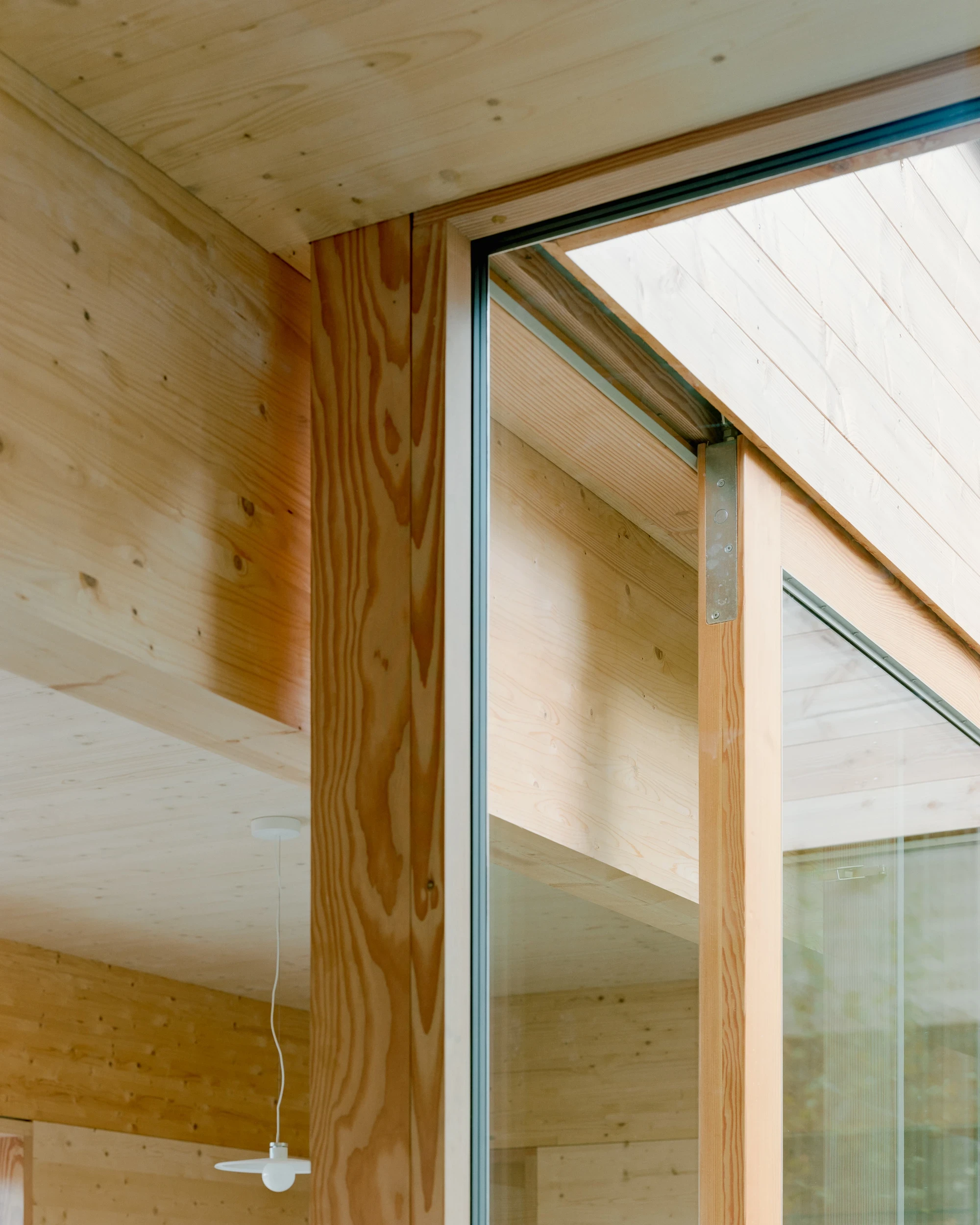 House in Ebeltoft by Høyer Arkitektur, photographed by Hampus Berndtson — detail of the sliding glass panel track recessed into the spruce CLT surround, a steel bracket at the corner junction and a white pendant lamp below.