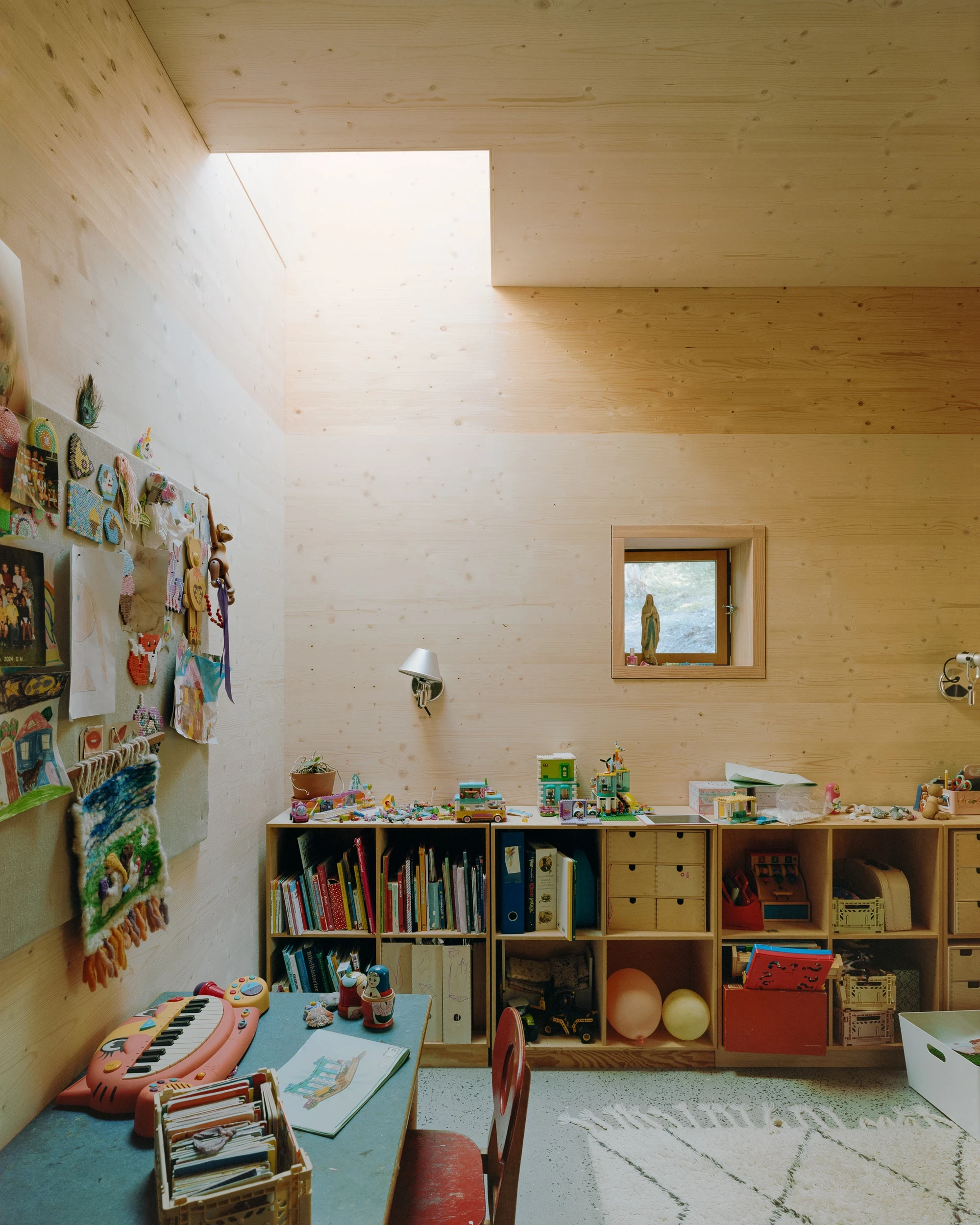 House in Ebeltoft by Høyer Arkitektur, photographed by Hampus Berndtson — a child's room with a rectangular ceiling rooflight casting diffused light on pale spruce CLT walls, a small square window set low, and built-in pine storage units.