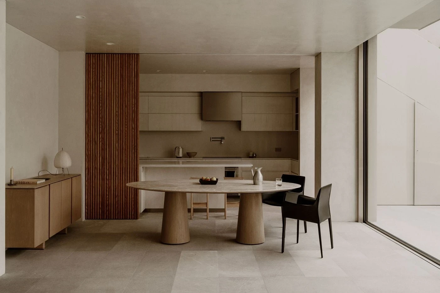 Barrancas by PPAA, photographed by Luis Garvan — the open-plan living area flows past a timber screen toward the travertine dining table, the garden visible through full-height glazing beyond.