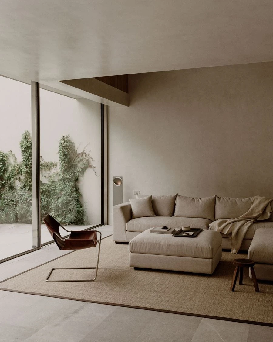 Barrancas by PPAA, photographed by Luis Garvan — a deep oatmeal sectional on a sisal rug faces full-height glazing onto the rear garden, the sofa anchoring the room while glass holds everything else open.