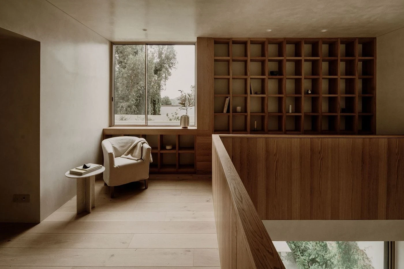 Barrancas by PPAA, photographed by Luis Garvan — a linen-slip armchair in a corner of natural plaster beside an oak bookcase, diffused light holding the surfaces at an even temperature.