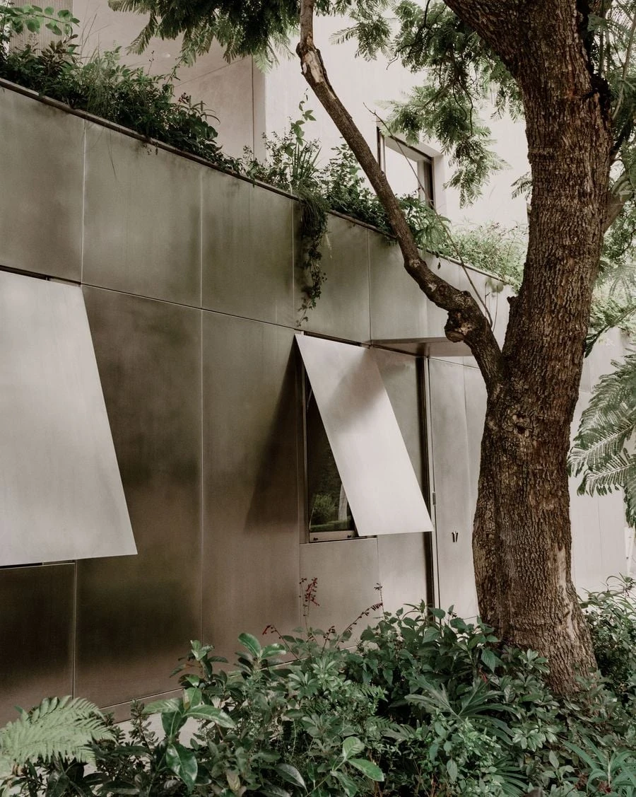Barrancas by PPAA, photographed by Luis Garvan — a pivoting metallic panel above a window reveals the mechanism of a facade that treats openings as interruptions to be concealed rather than celebrated.