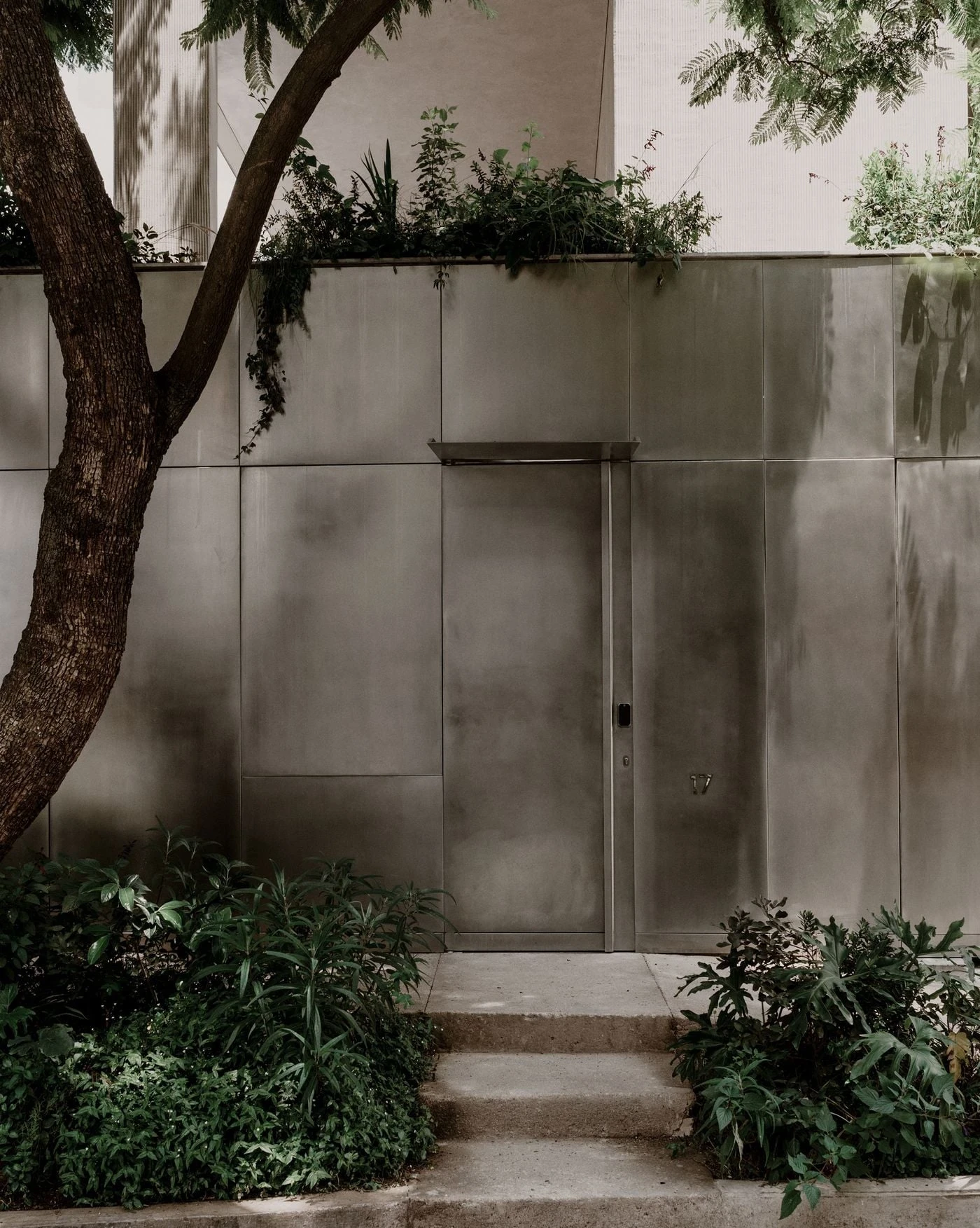 Barrancas by PPAA, photographed by Luis Garvan — the matte metallic perimeter wall reads flush at street level, the house number 17 the only mark interrupting an otherwise seamless plane.