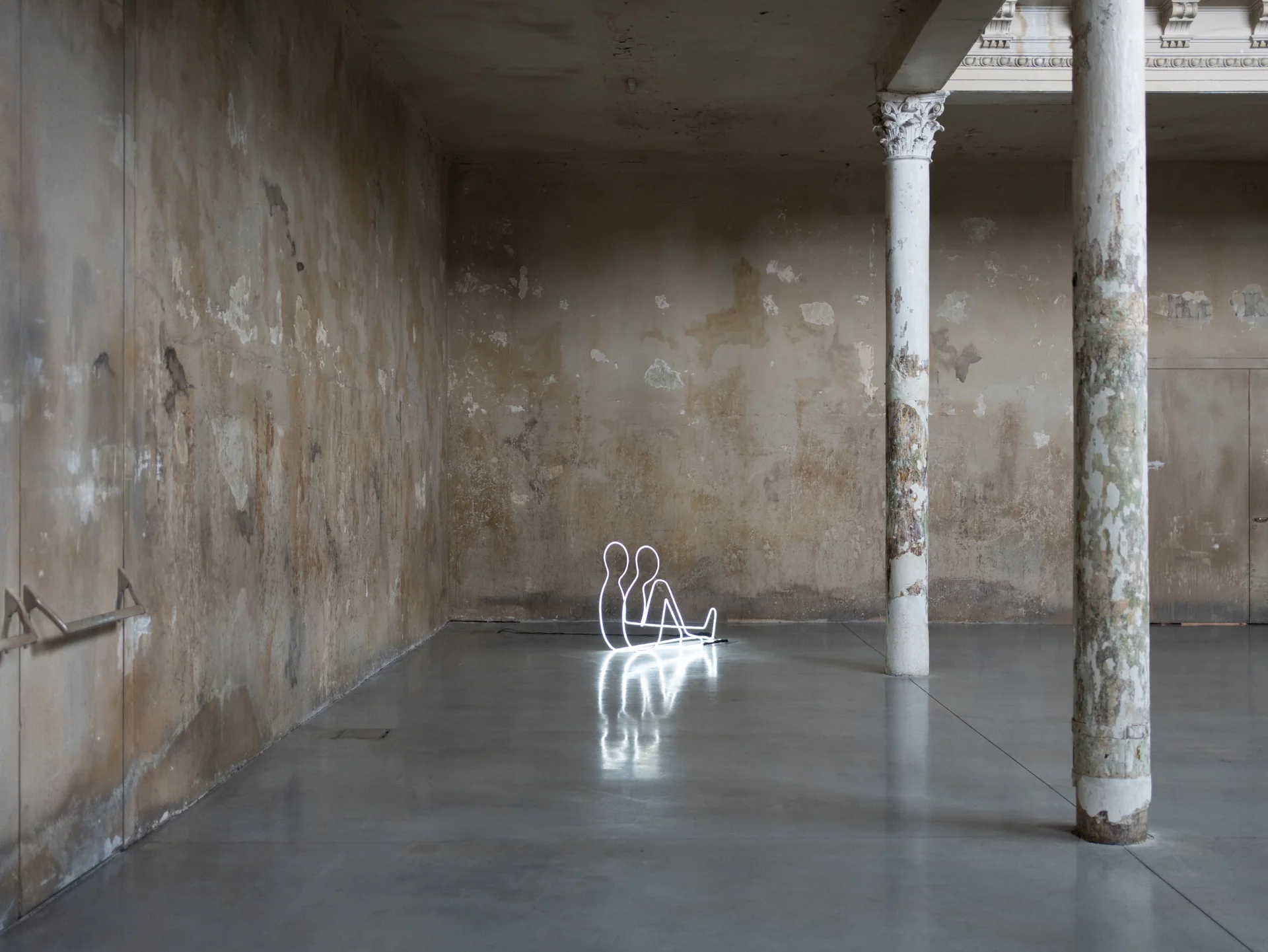 Everything Comes Together While Pushing All Apart by Roxana Morar — Neon outline of two figures sitting side by side by Albert Kaan glowing on a polished floor in a long room of peeled walls and bare Corinthian columns.