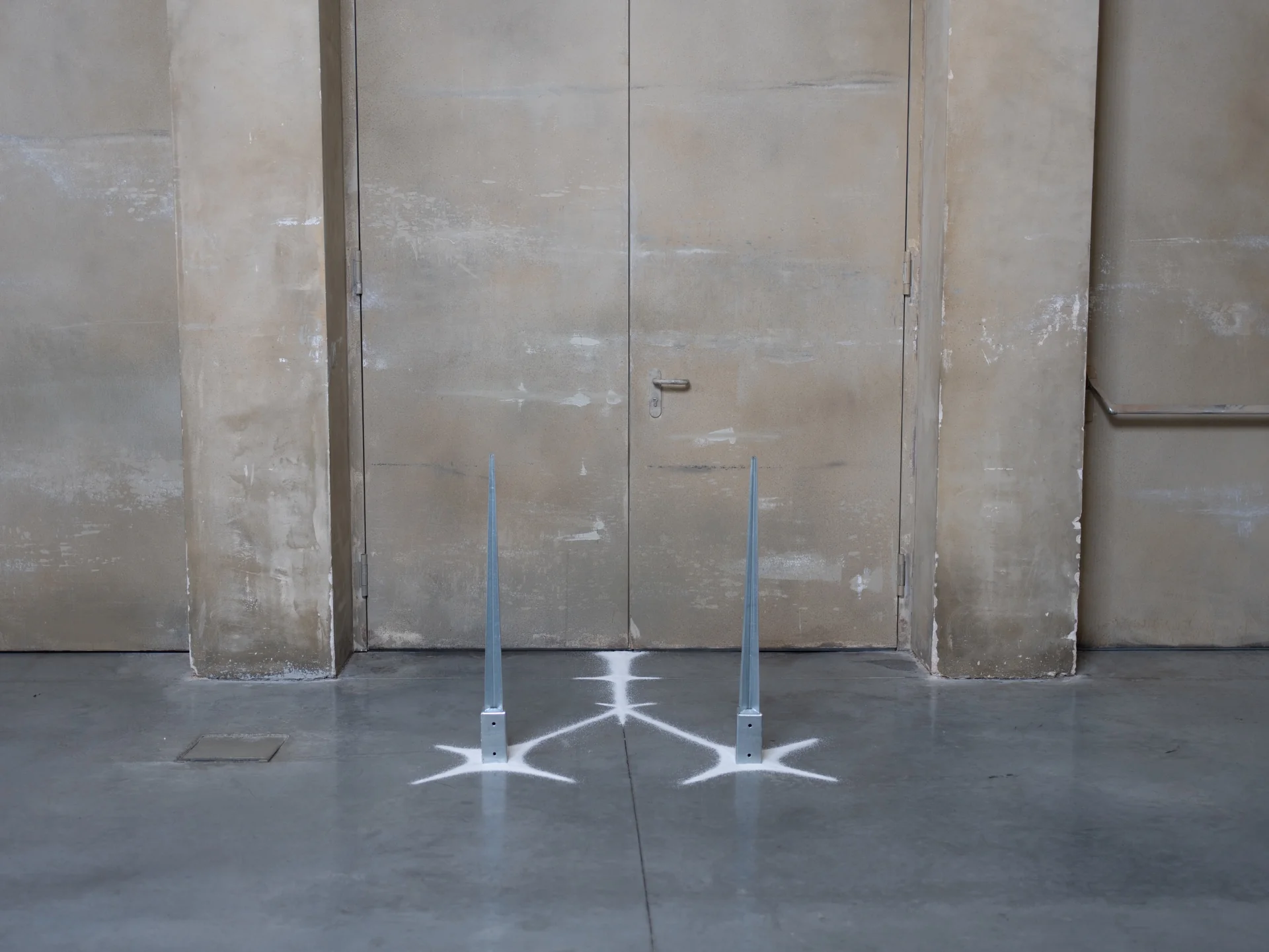 Everything Comes Together While Pushing All Apart by Roxana Morar — Two galvanized spike stakes by Ana Ionescu rooted to the floor with white painted starbursts, set in front of double doors stained the colour of old plaster.