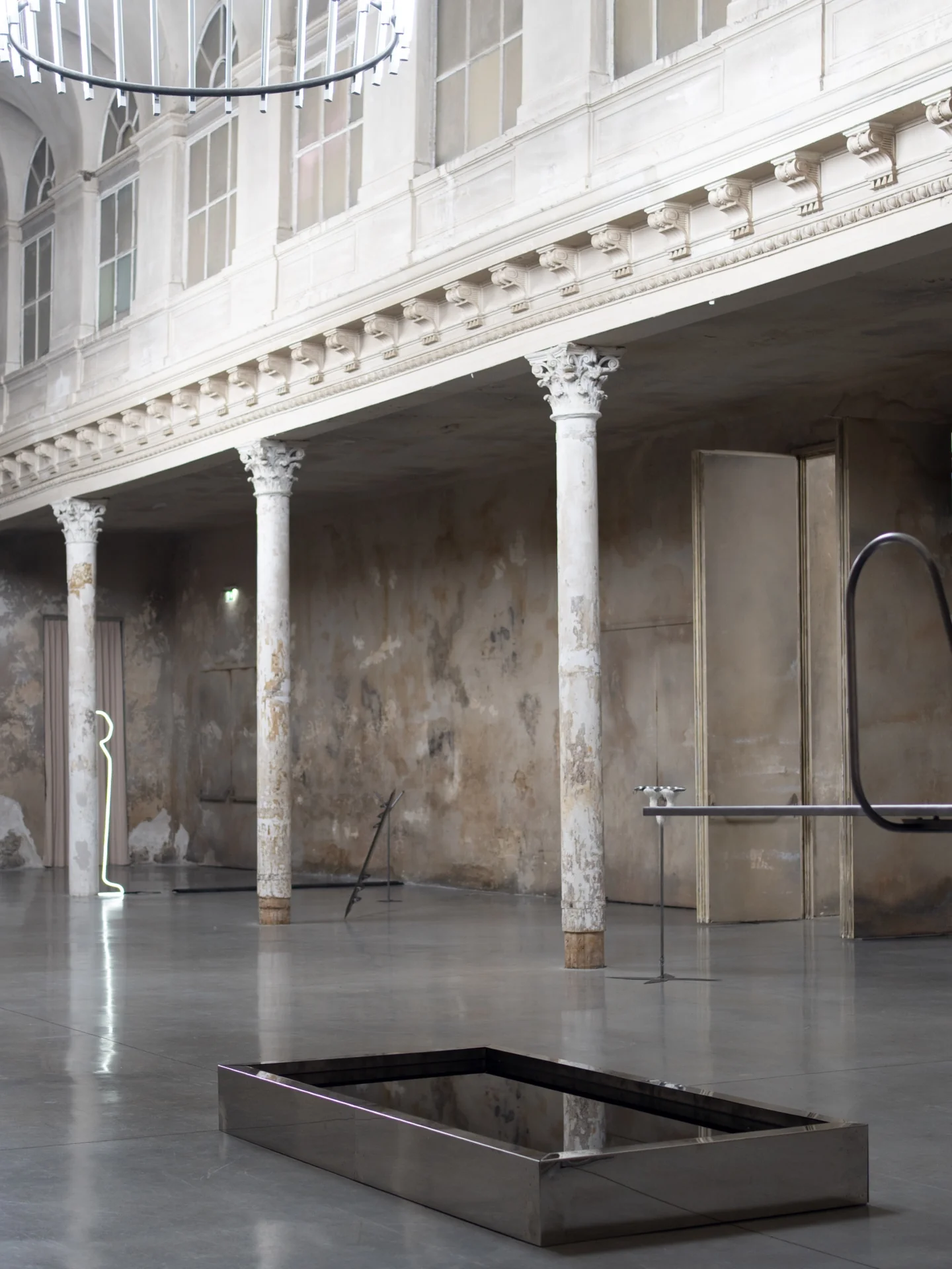 Everything Comes Together While Pushing All Apart by Roxana Morar — Albert Kaan's arched piping and Ana Ionescu's small neon figure framed by Reaktor Wien's two-tier loggia, mirror trough collecting the ceiling at floor level.