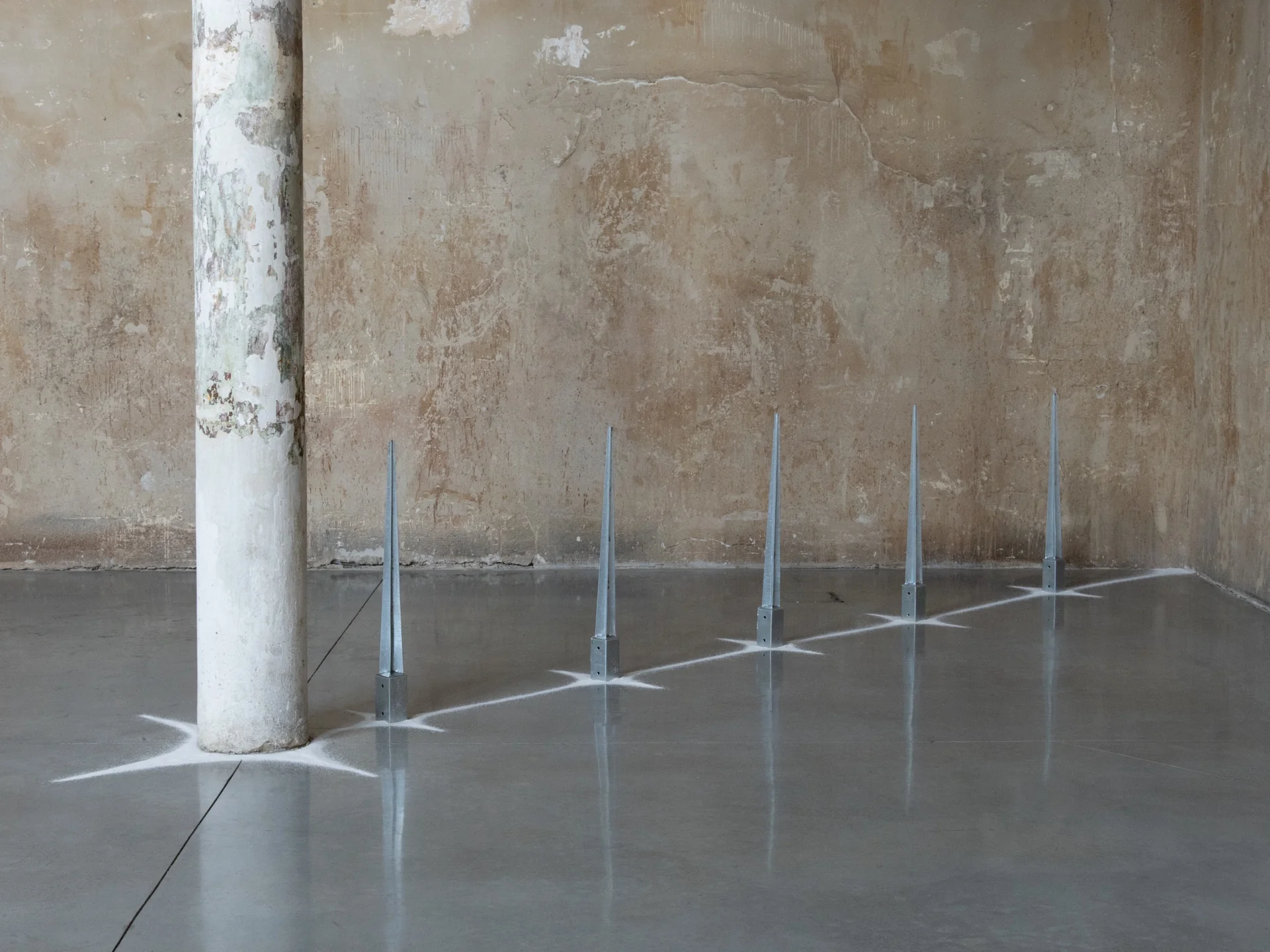 Everything Comes Together While Pushing All Apart by Roxana Morar — Five steel spikes by Ana Ionescu lined up against the worn lime-plaster wall, painted starbursts radiating from each base across the polished floor.