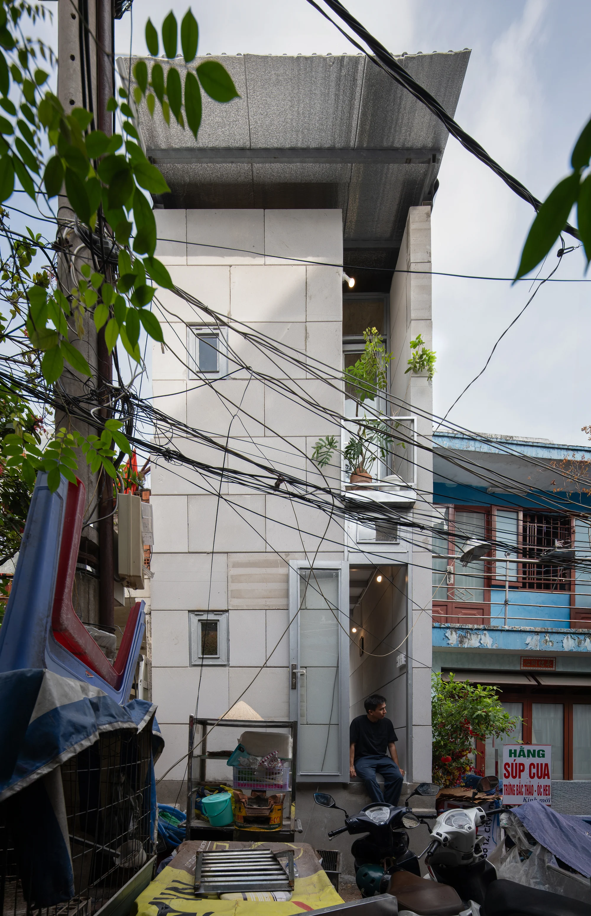 11M2 HOUSE by scale50, photographed by Nguyen Manh Toan — Rear elevation against accumulated brick walls, corrugated metal sheds and salvaged doors of the canal block.