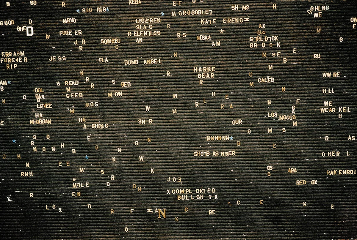 Christopher Postlewaite by Christopher Postlewaite, photographed by Christopher Postlewaite — The full grid of a felt letterboard from the former strip club Cousin Danny's, scrambled white capitals on black, names and half-sentences arranged as…