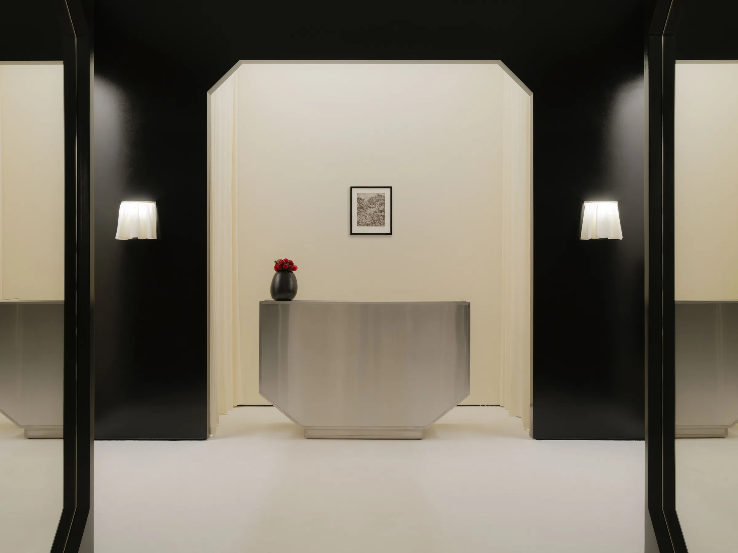 Roses Lace by EDXXKAT — Frontal shot of the cash desk recess: glossy black walls open to a tall white niche holding the brushed-steel desk, a small framed monochrome print above and a black vase of red roses set on the desk surface.
