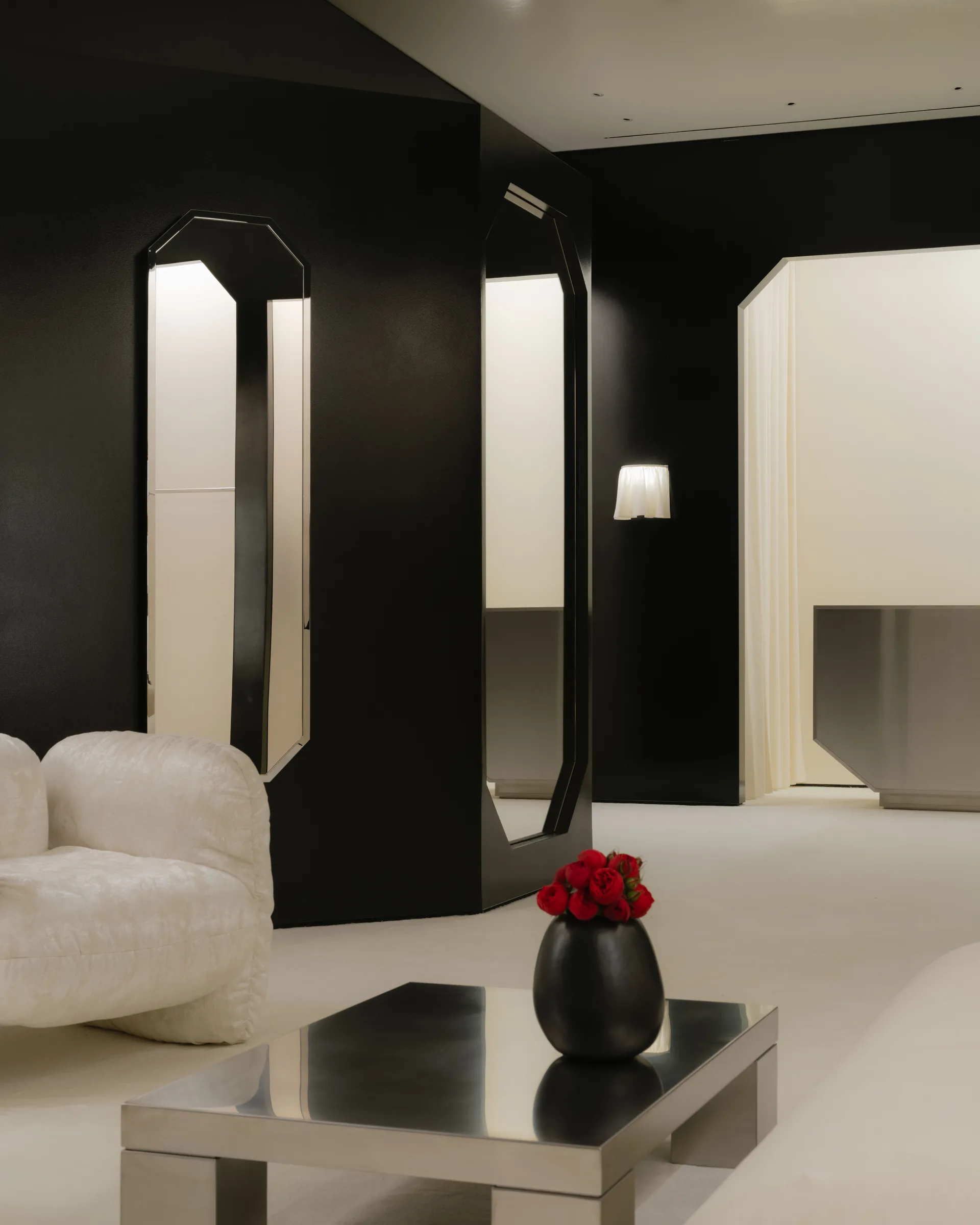 Roses Lace by EDXXKAT — A pair of octagonal black floor mirrors hinged at the centre of the lounge, a black-vased red rose on a brushed-metal cube table in the foreground and the curve of a white shearling sofa just visible at left.