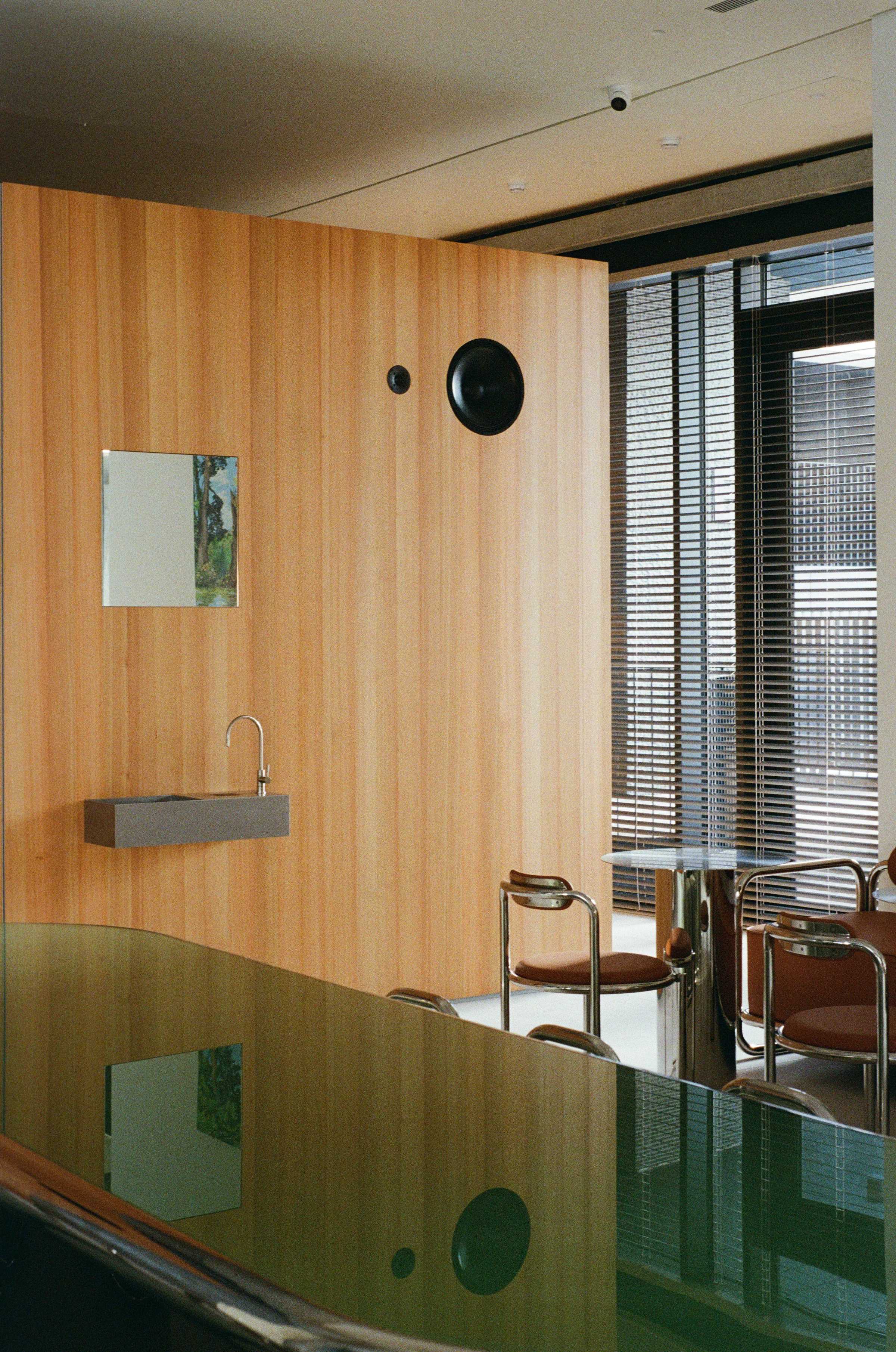 Nothing Fancy by EDXXKAT — Concrete column and shared table: weathered grey concrete fills the upper frame, brown leather seats line up at the laminate communal table on the left, the surface lit from above by warm daylight.