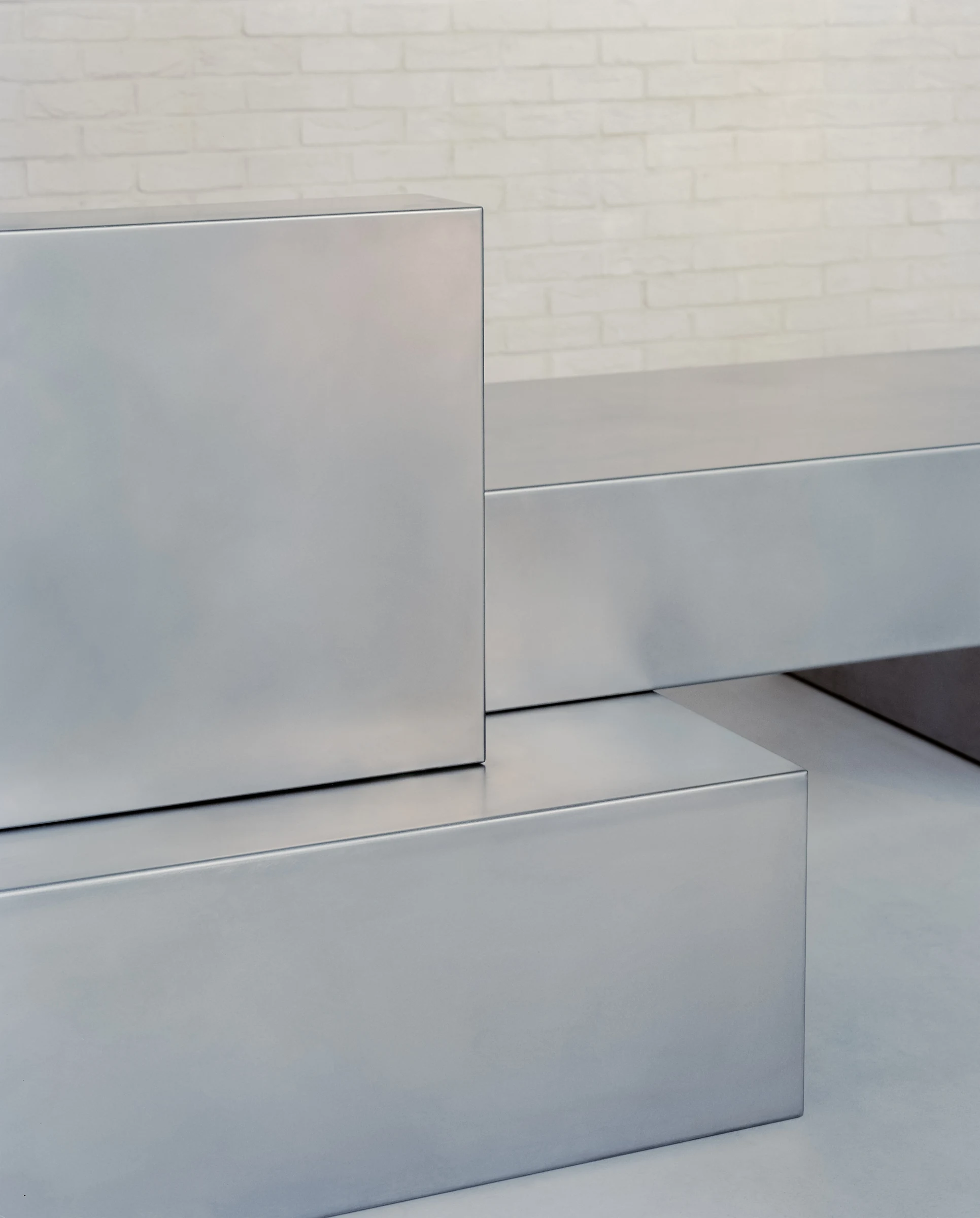 Cherry Orchard by Actual Office, photographed by Nick Dearden — Top-down detail of the concierge desk: a perfectly circular drop-point cut into the stainless steel surface, the joinery and welds reading clean against the pale concrete floor below.
